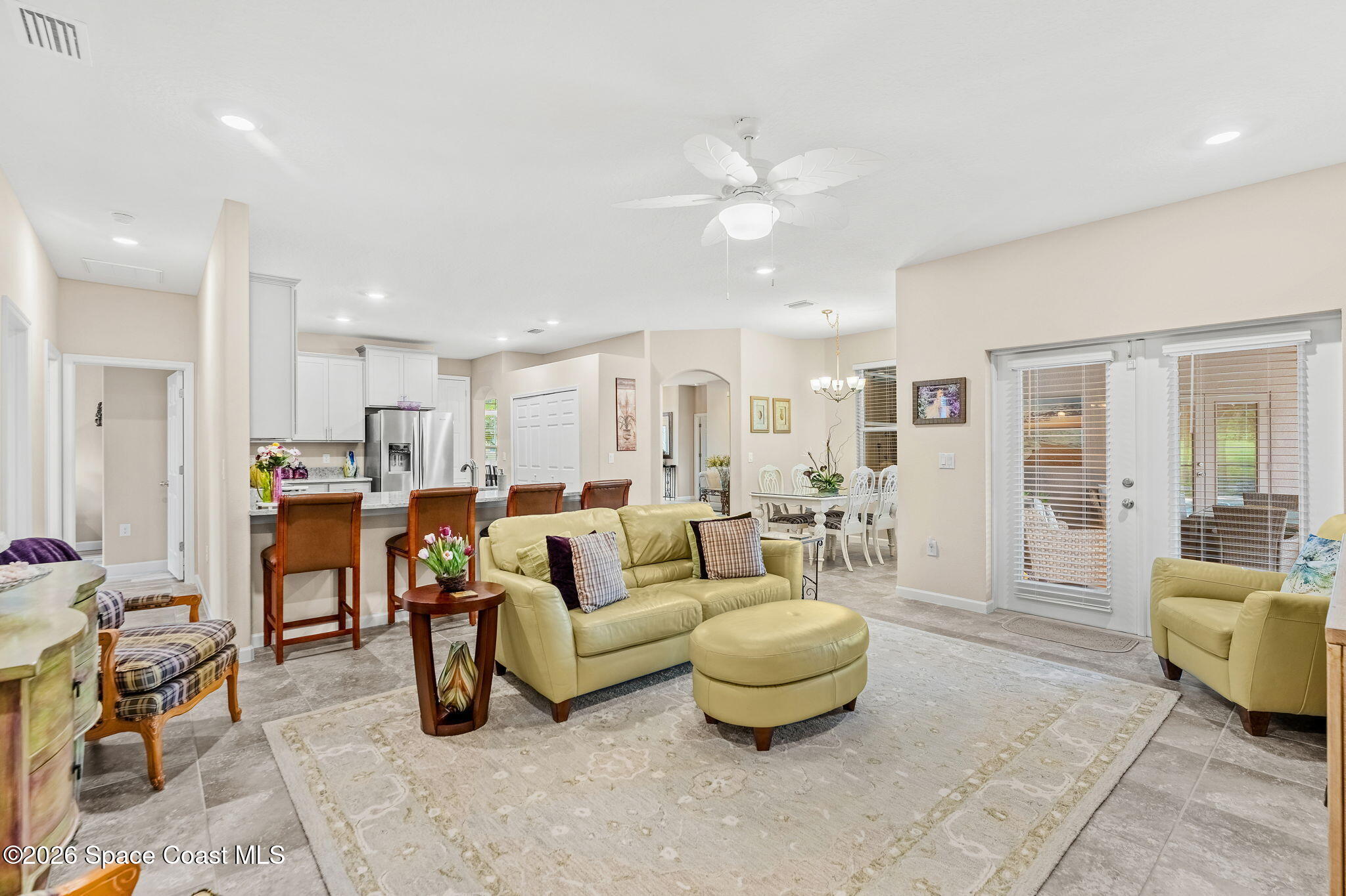 Open-plan living room with pale green seating, a kitchen breakfast bar, and glass patio doors.