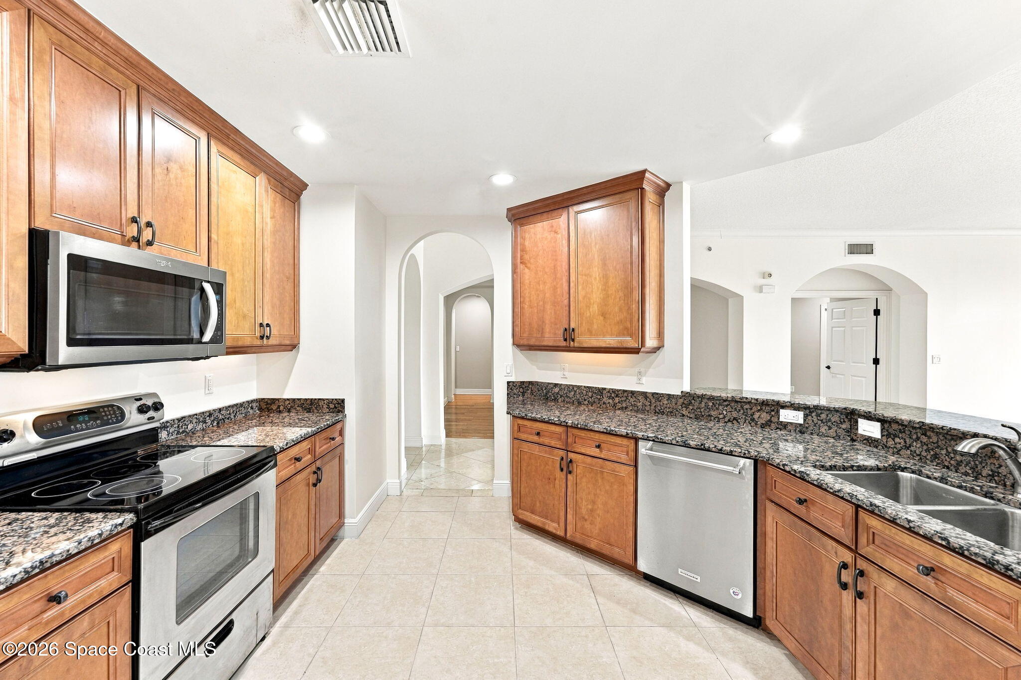 Kitchen with wood cabinets, granite counters, stainless appliances, and arched openings.