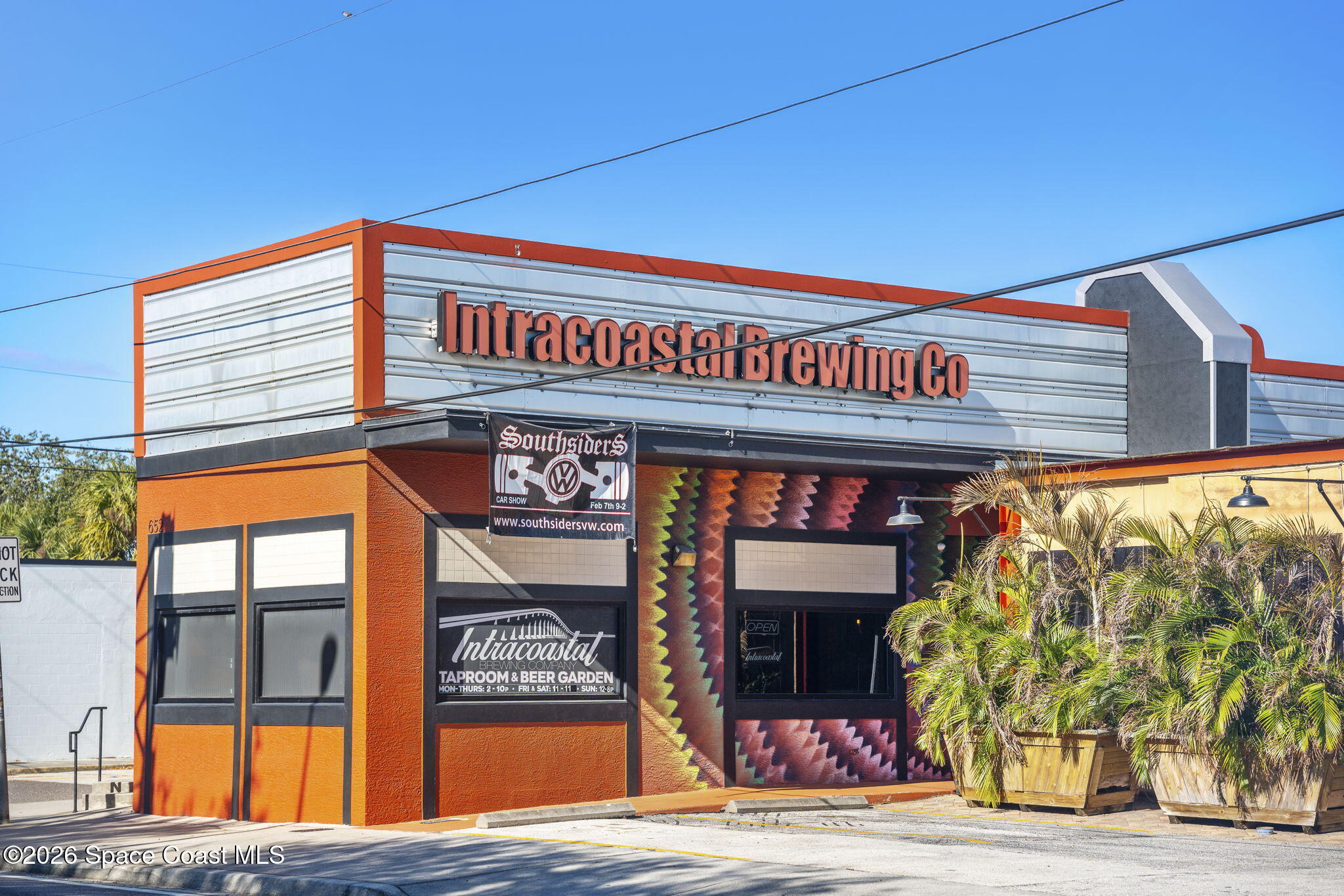 Intracoastal Brewing Co. storefront with orange facade, colorful mural, and palm planters.