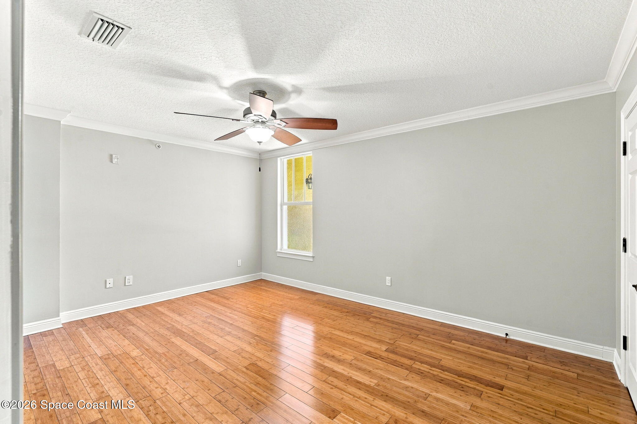 Vacant room with warm wood flooring, gray walls, ceiling fan, and a single window.