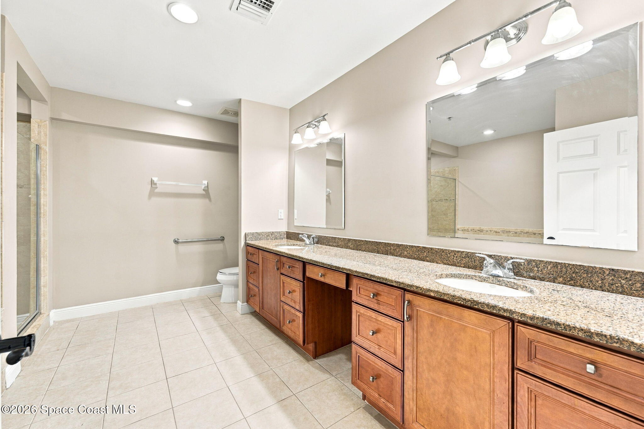 Bathroom with a long double-sink granite vanity, wood cabinets, and a glass-enclosed shower.