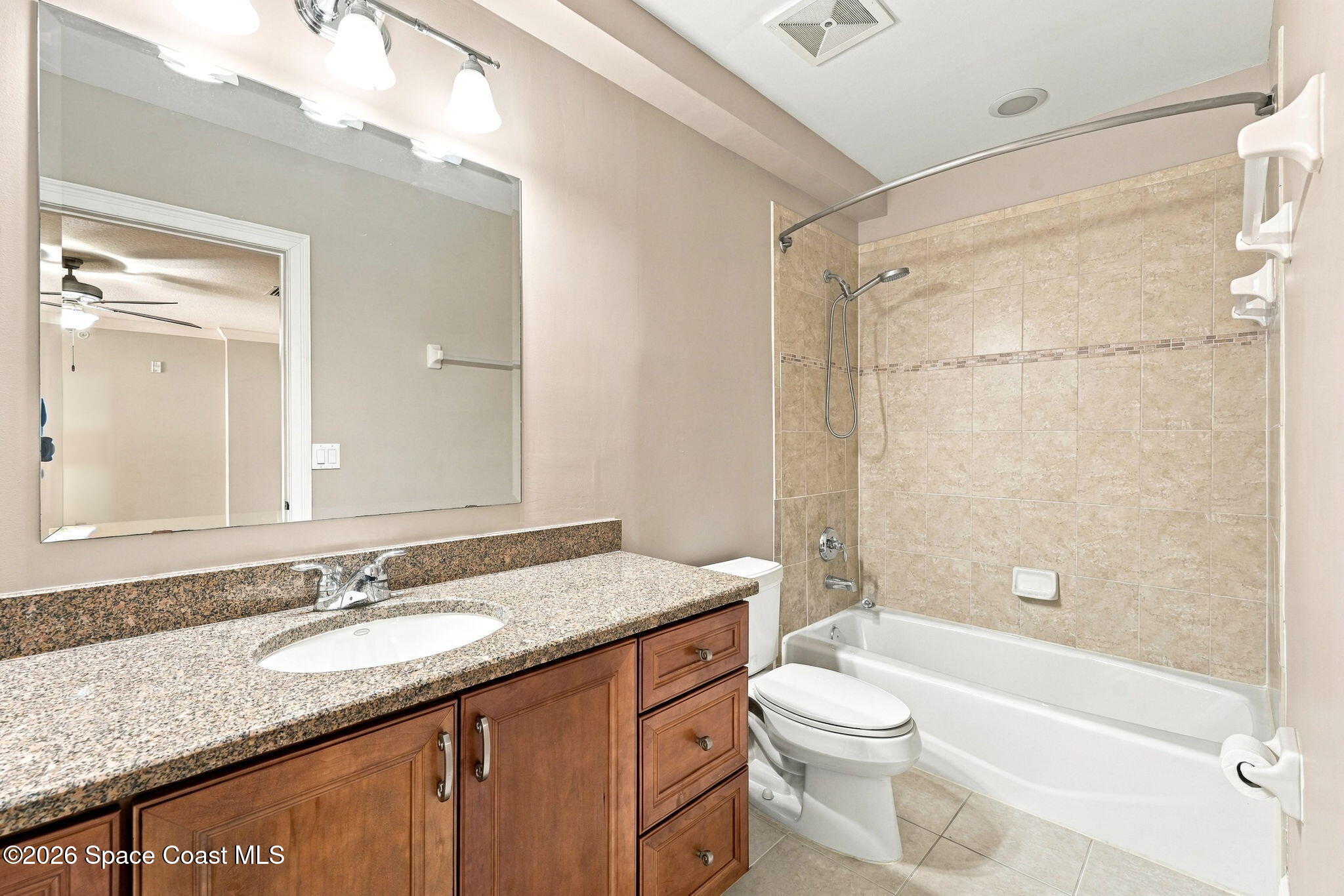 Bathroom with granite vanity, wooden cabinets, and a tiled tub and shower.