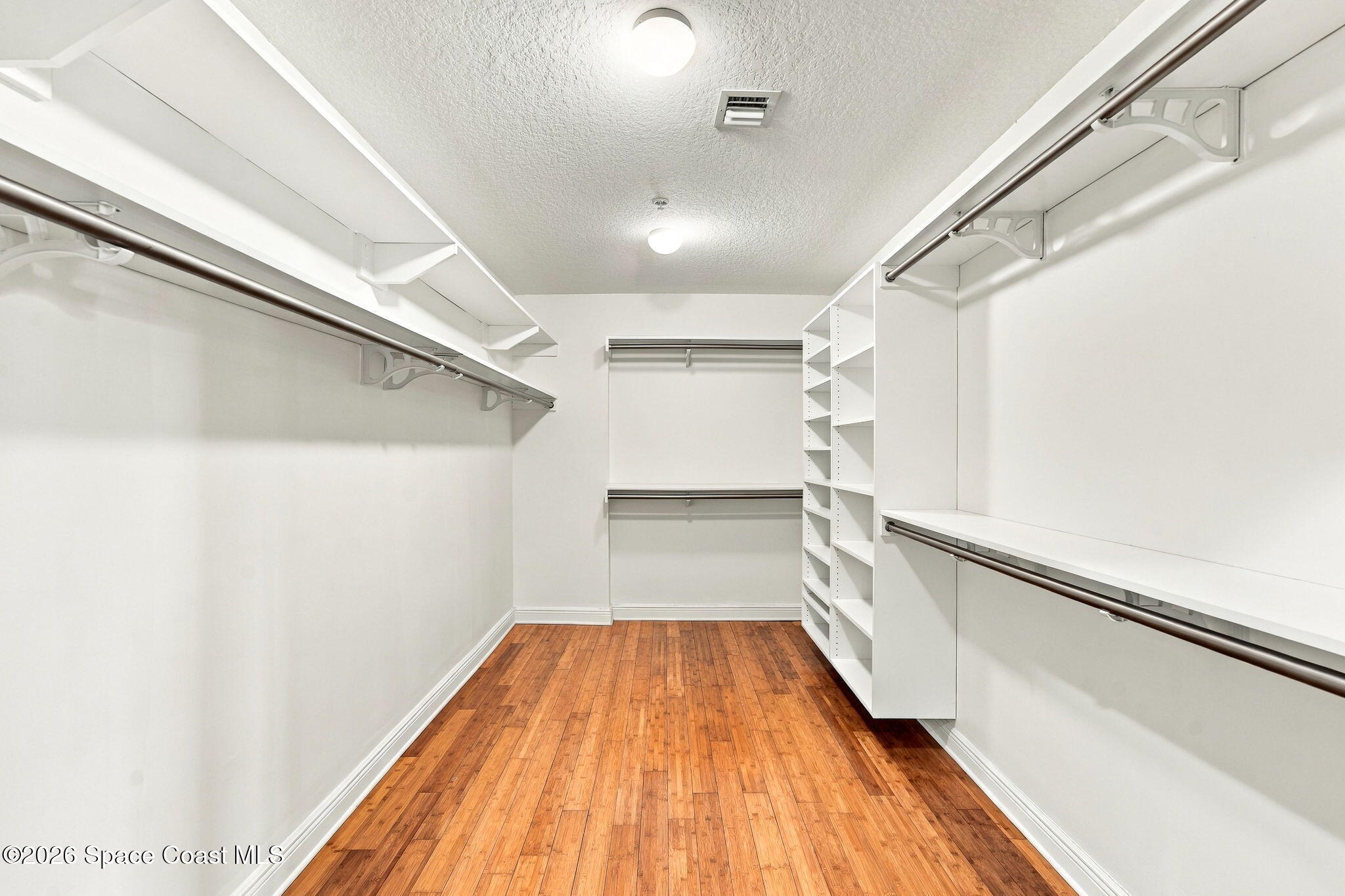 Walk-in closet with built-in white shelving, hanging rods, and a wood plank floor.