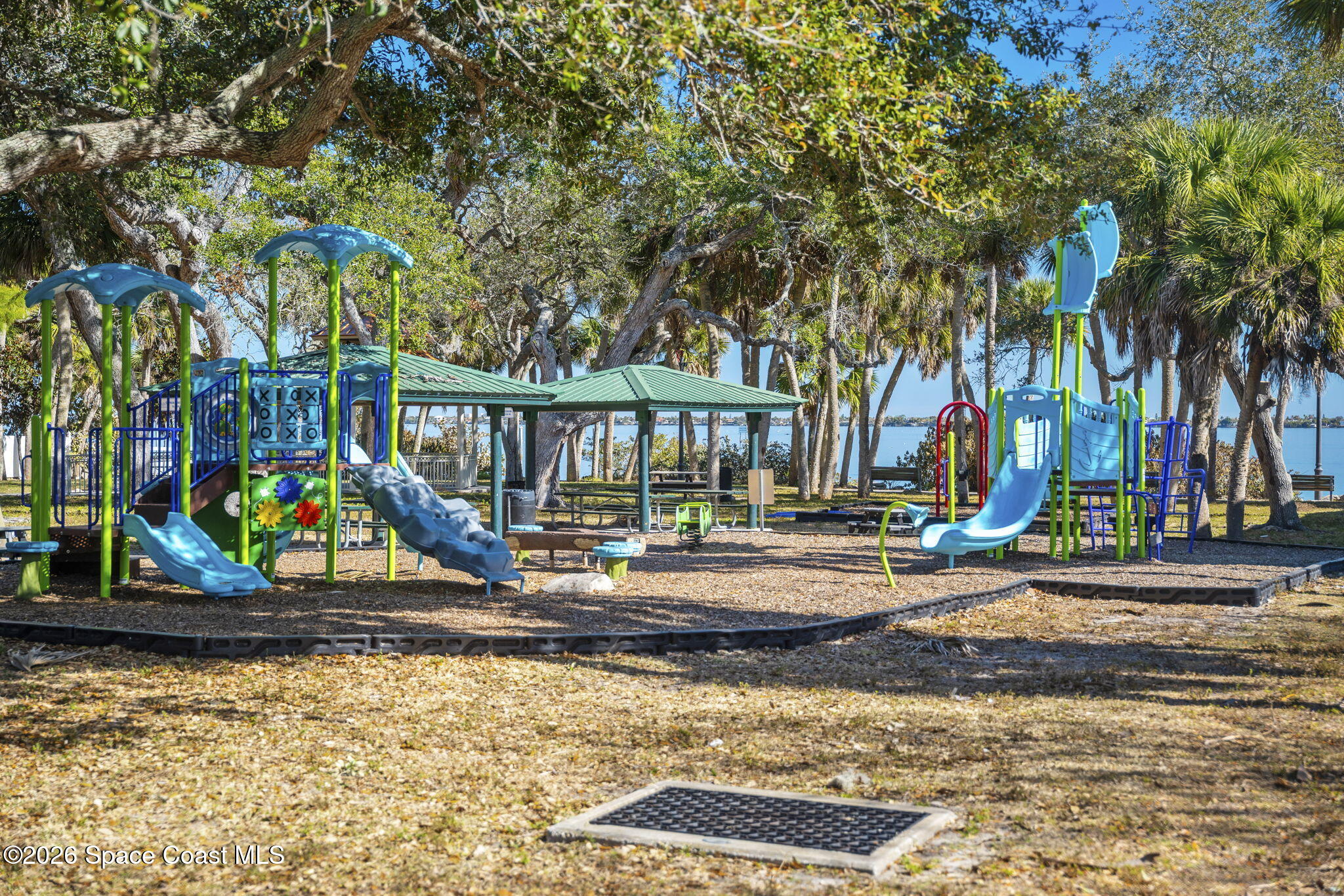 Waterfront playground with blue slides, climbing structures, and shaded picnic shelters.