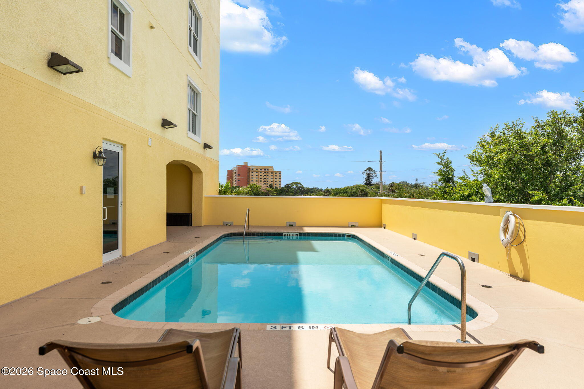 Outdoor pool beside a yellow building, with lounge chairs and a metal ladder.