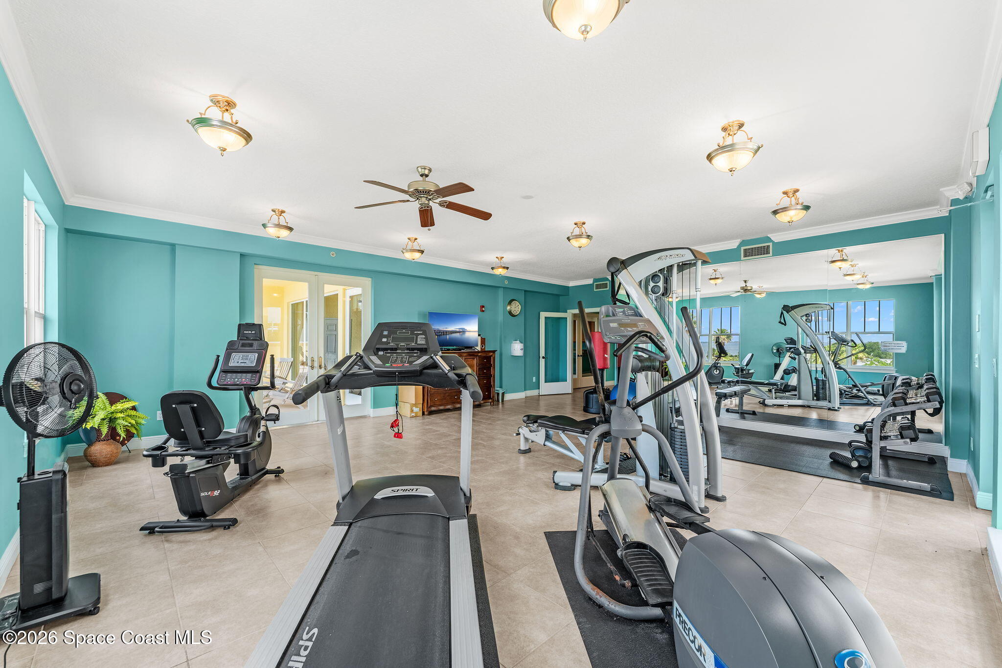 Fitness room with treadmills and strength equipment, turquoise walls, and a mirrored wall.