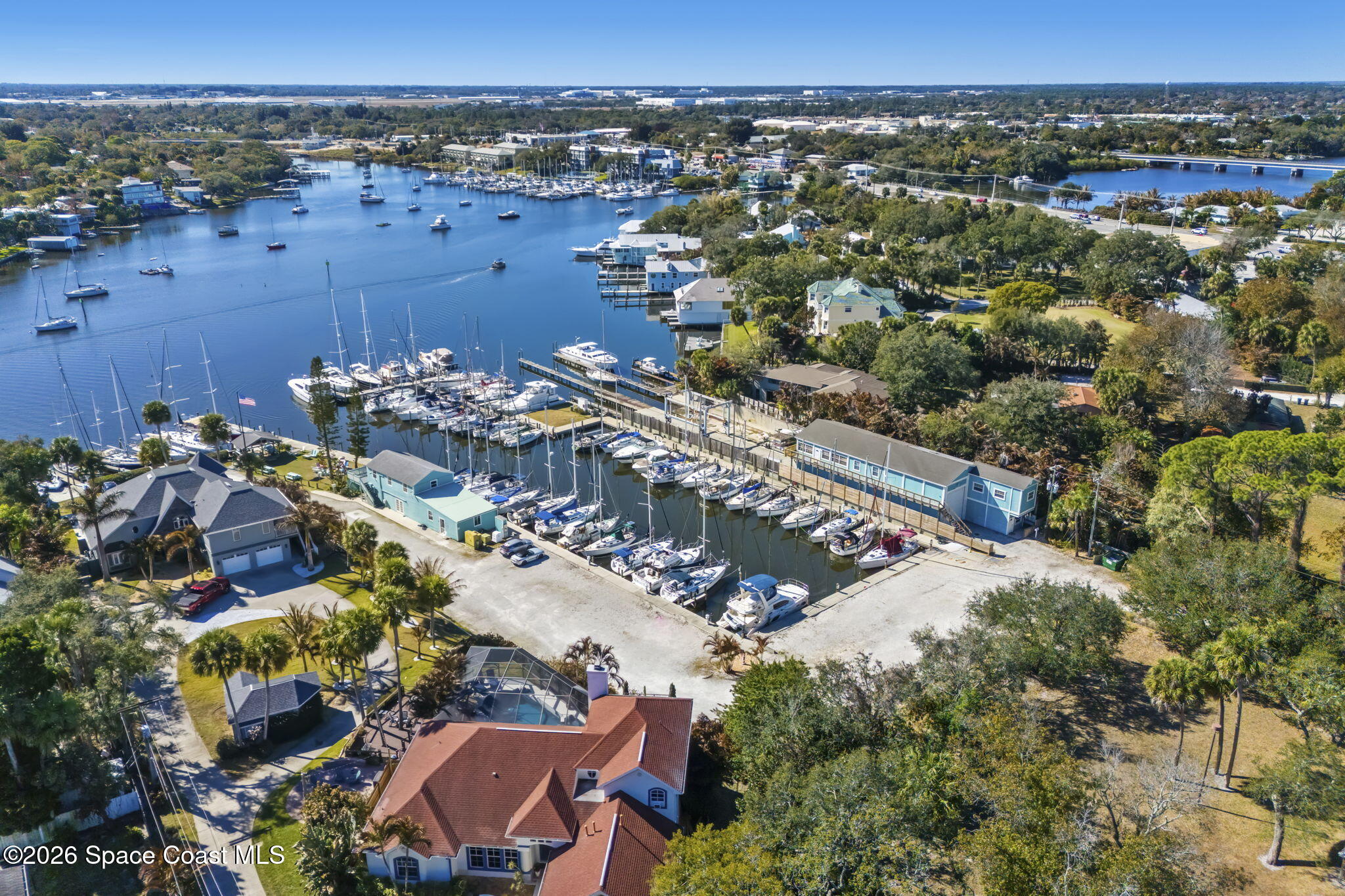 Aerial marina with rows of docked sailboats and waterfront homes along a tree-lined waterway.