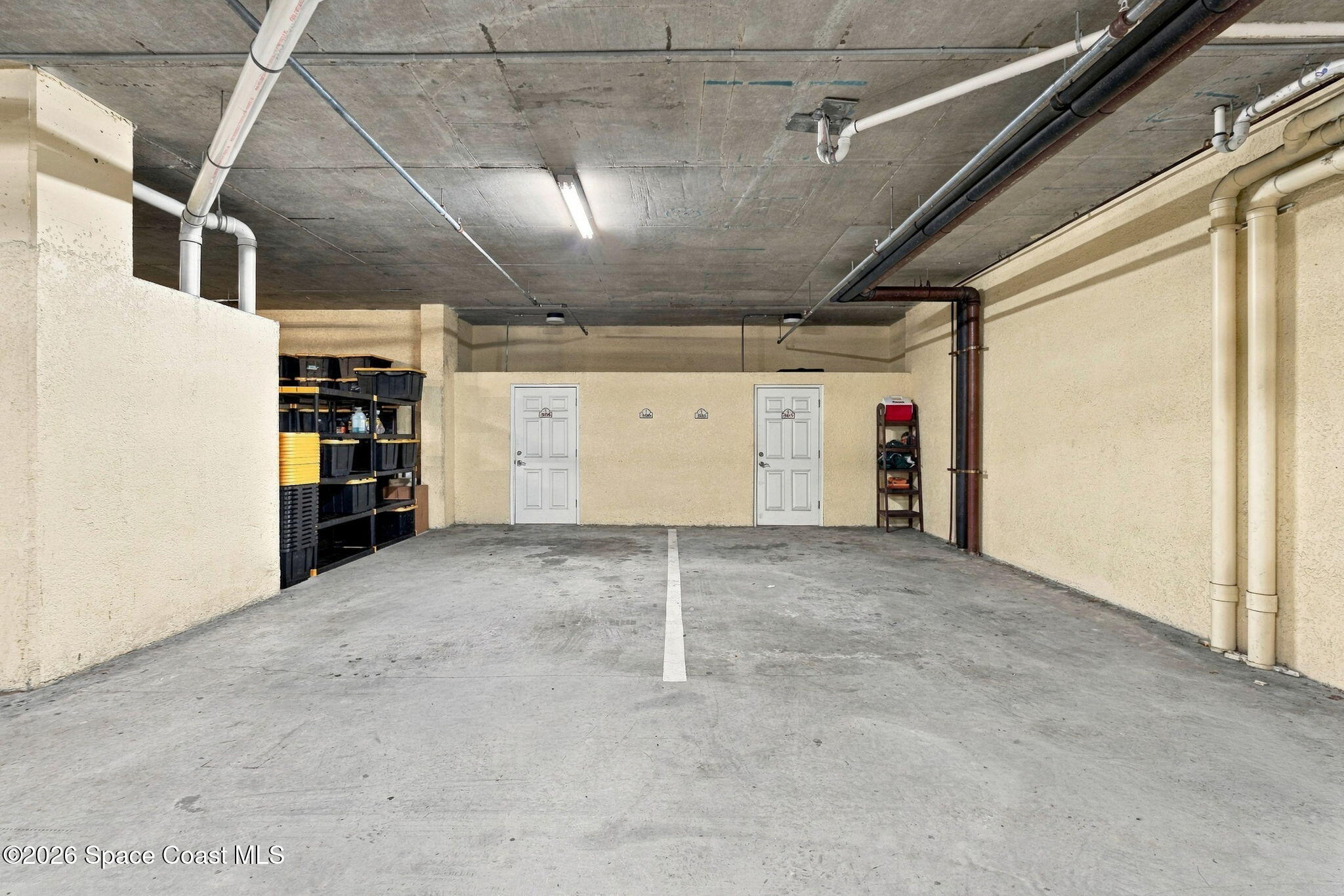 Interior parking and storage area with a marked concrete bay, exposed pipes, and shelving.