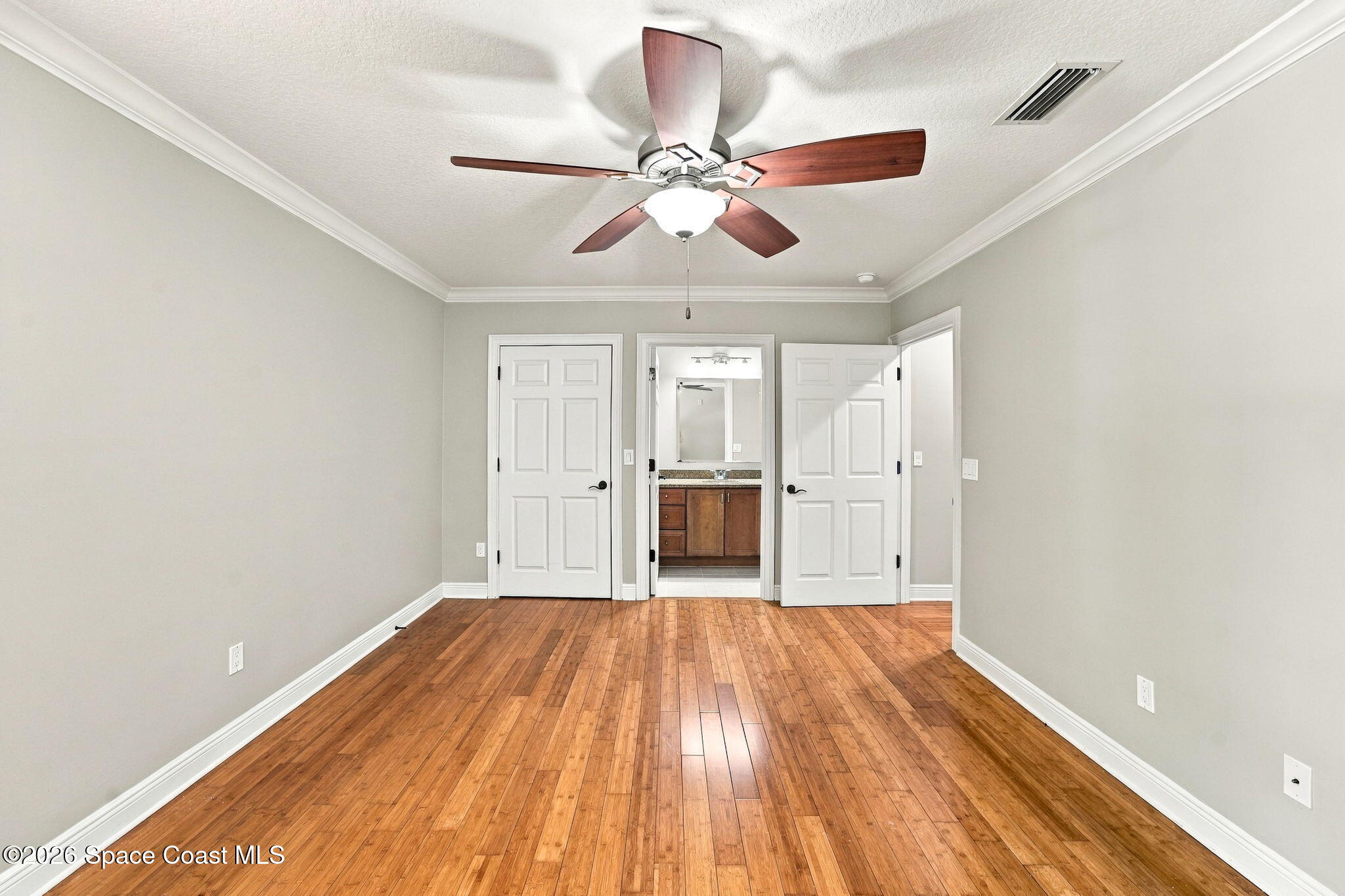 Empty bedroom with hardwood floors, a ceiling fan, and open doors to a bathroom and adjoining space.