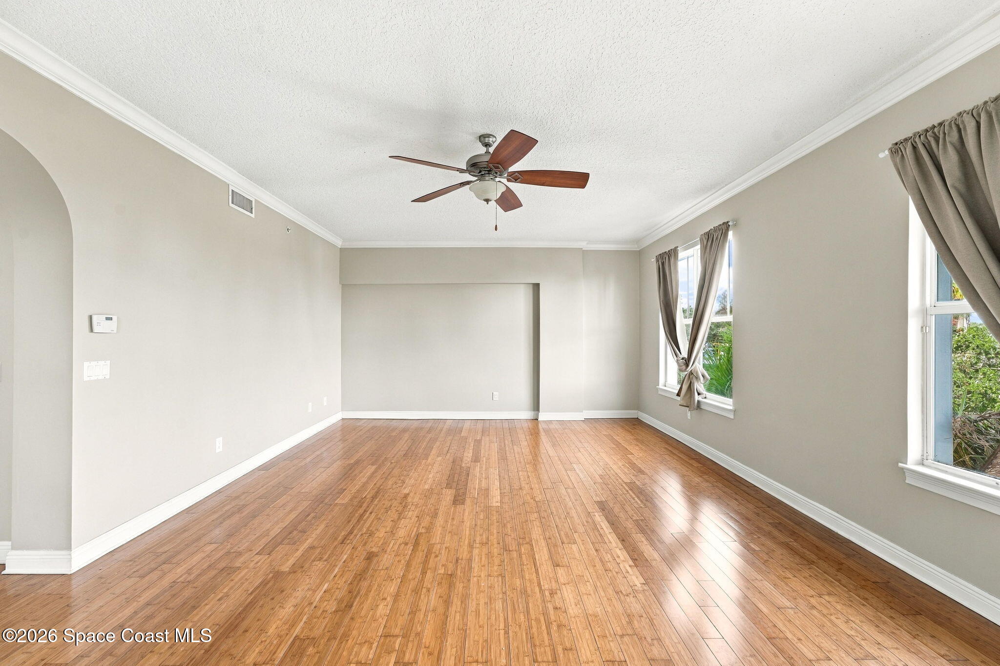 Empty living room with polished wood floors, curtained windows, and a ceiling fan.