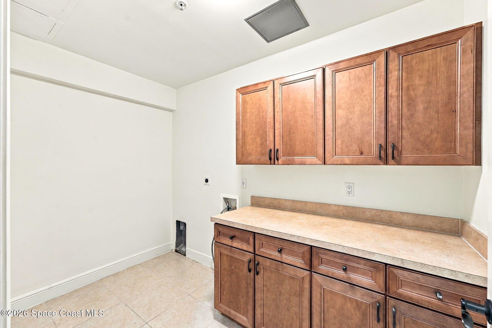 Laundry room with wood cabinets, a long countertop, and tile flooring.