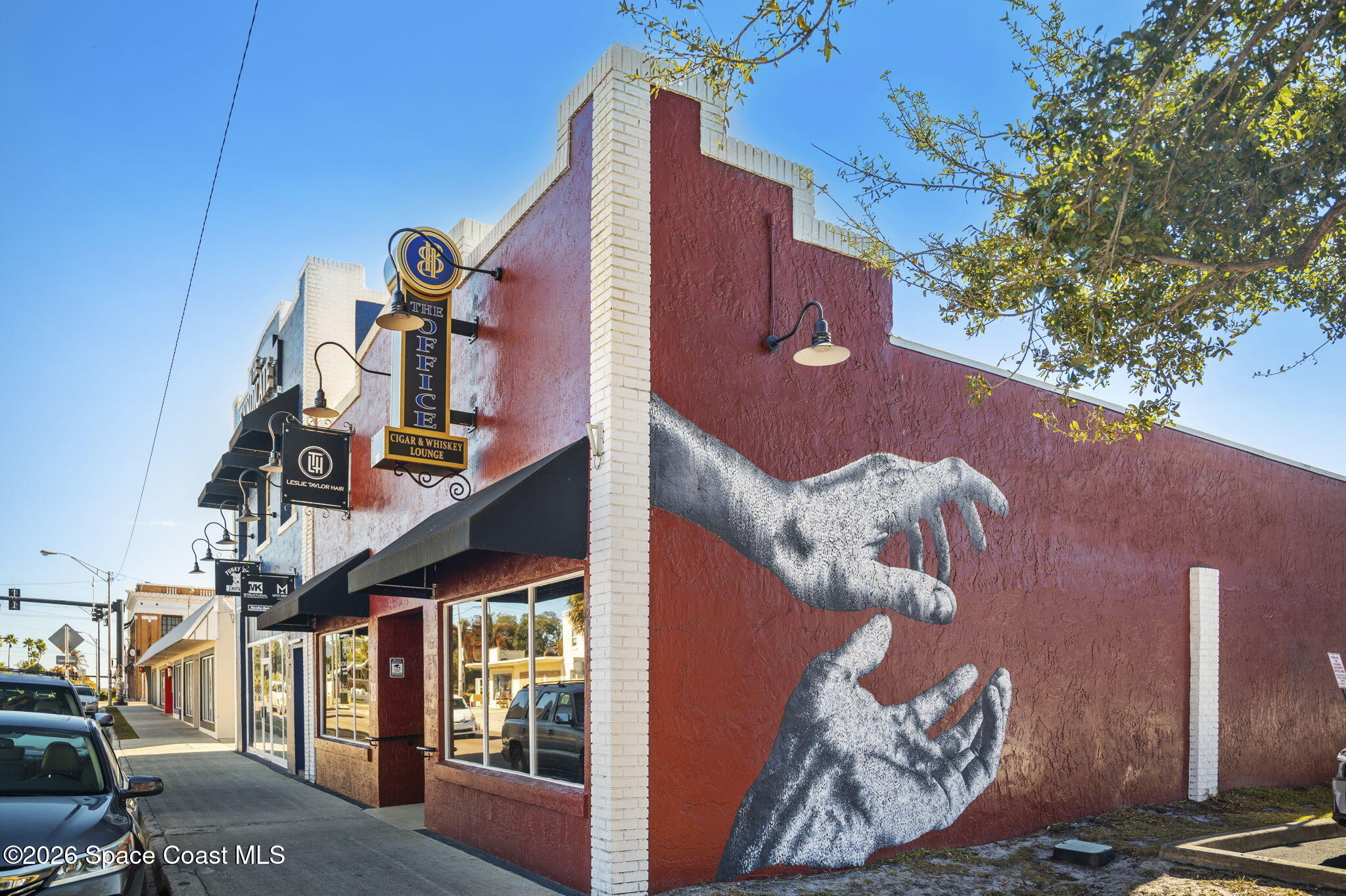 Commercial storefront with a large mural of reaching hands on its red side wall.