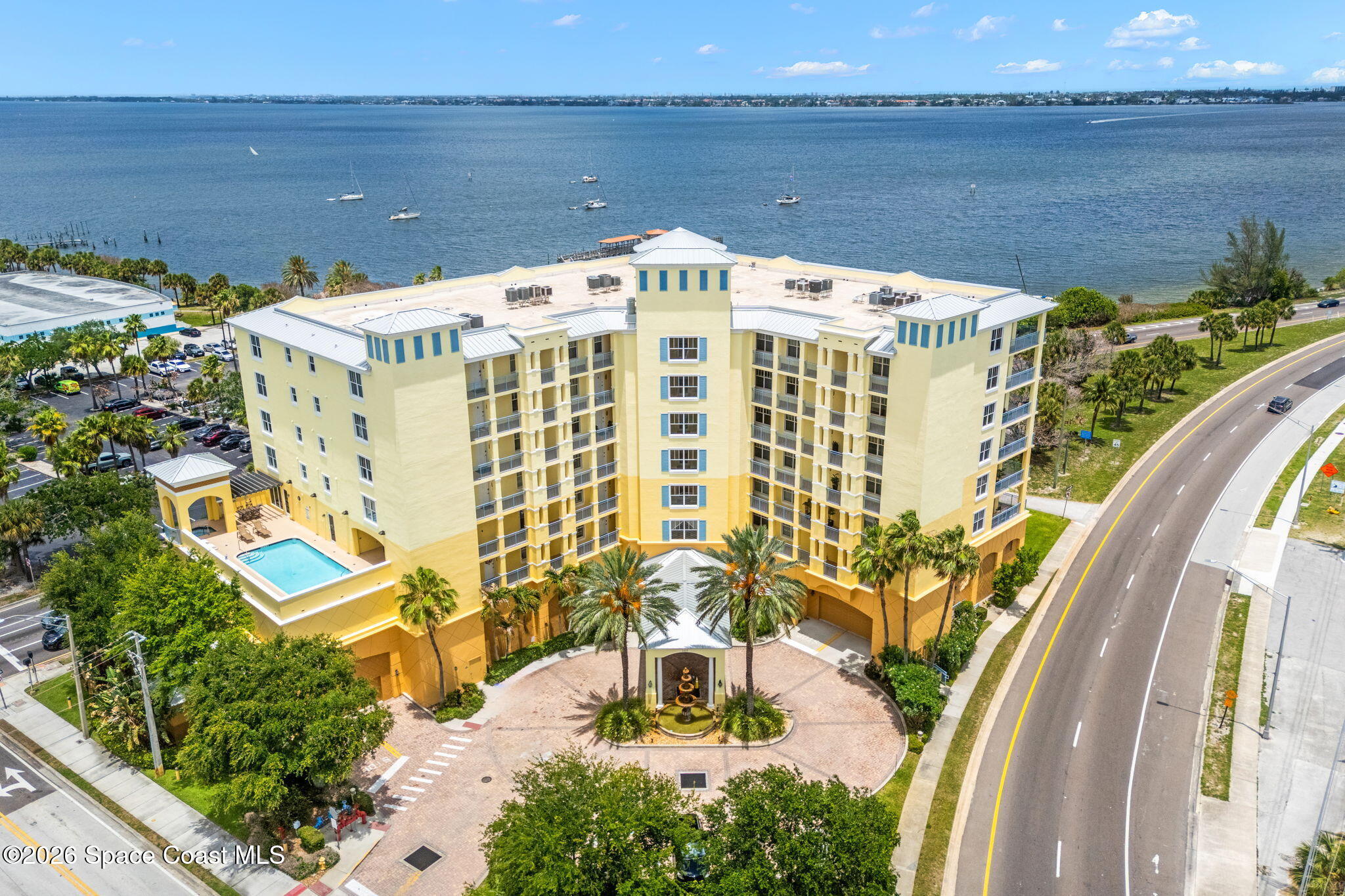 Waterfront condominium with a raised pool, courtyard fountain, and boats on the water behind it.