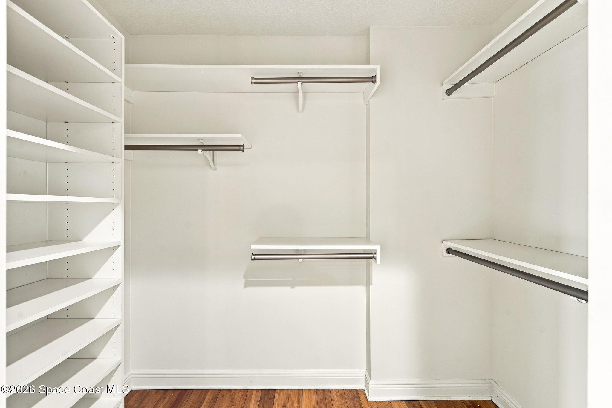 Walk-in closet with built-in white shelving, multiple hanging rods, and hardwood flooring.
