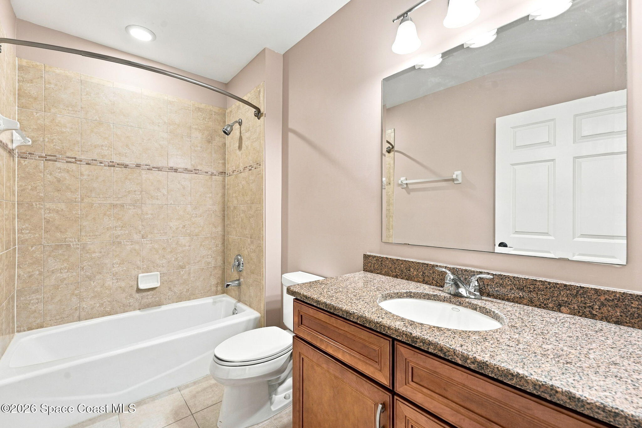Bathroom with a tiled tub and shower, toilet, and wood vanity with a granite countertop.
