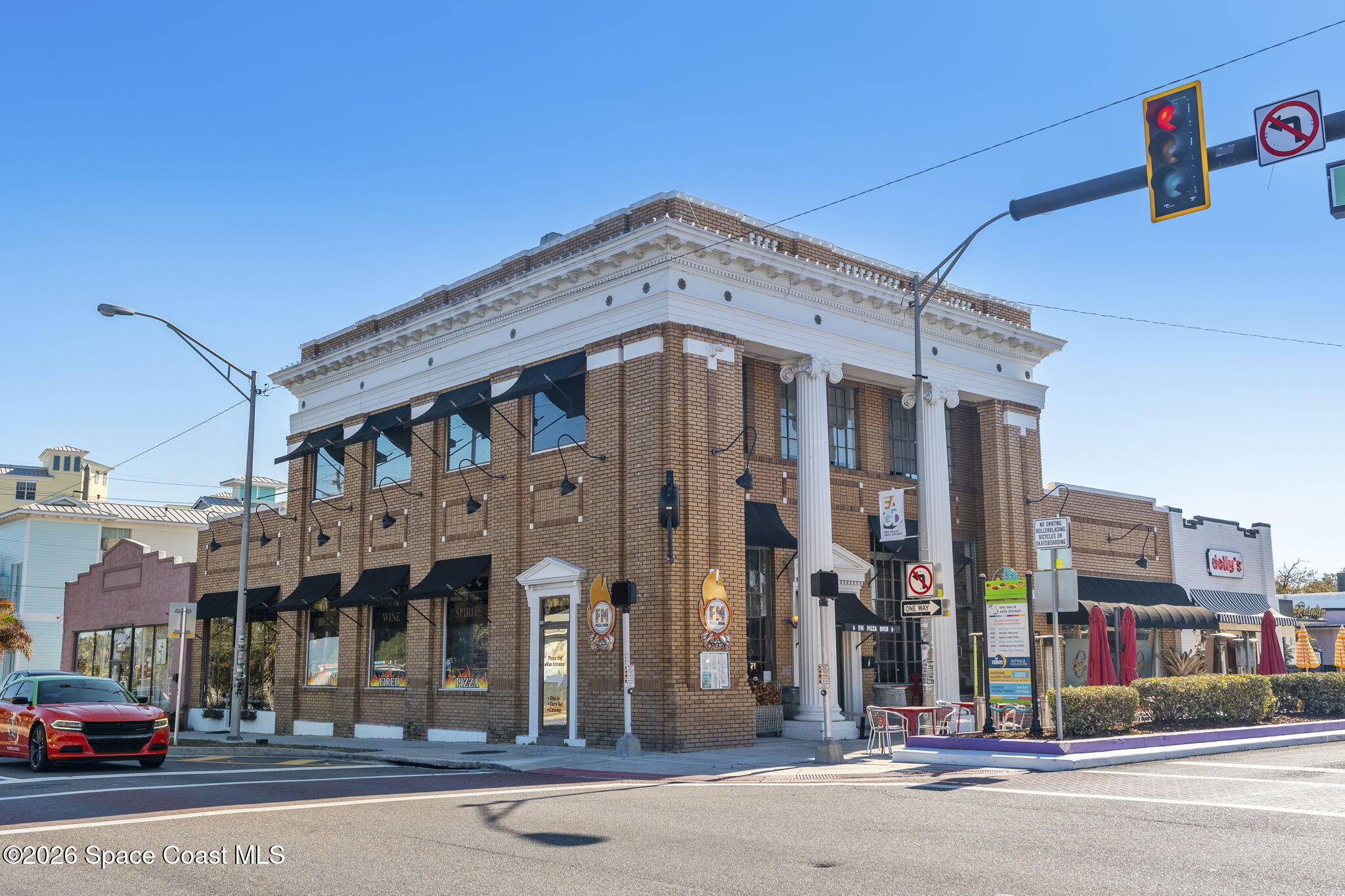 Two-story brick commercial building with white columns, black awnings, and sidewalk dining at a downtown intersection.