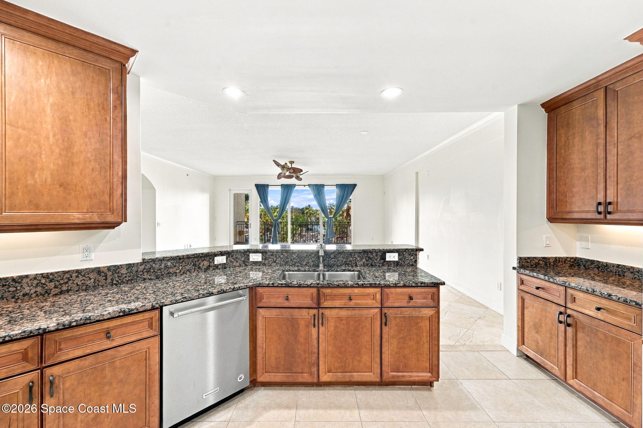 Kitchen with warm wood cabinets and granite counters, opening toward a palm-lined balcony.