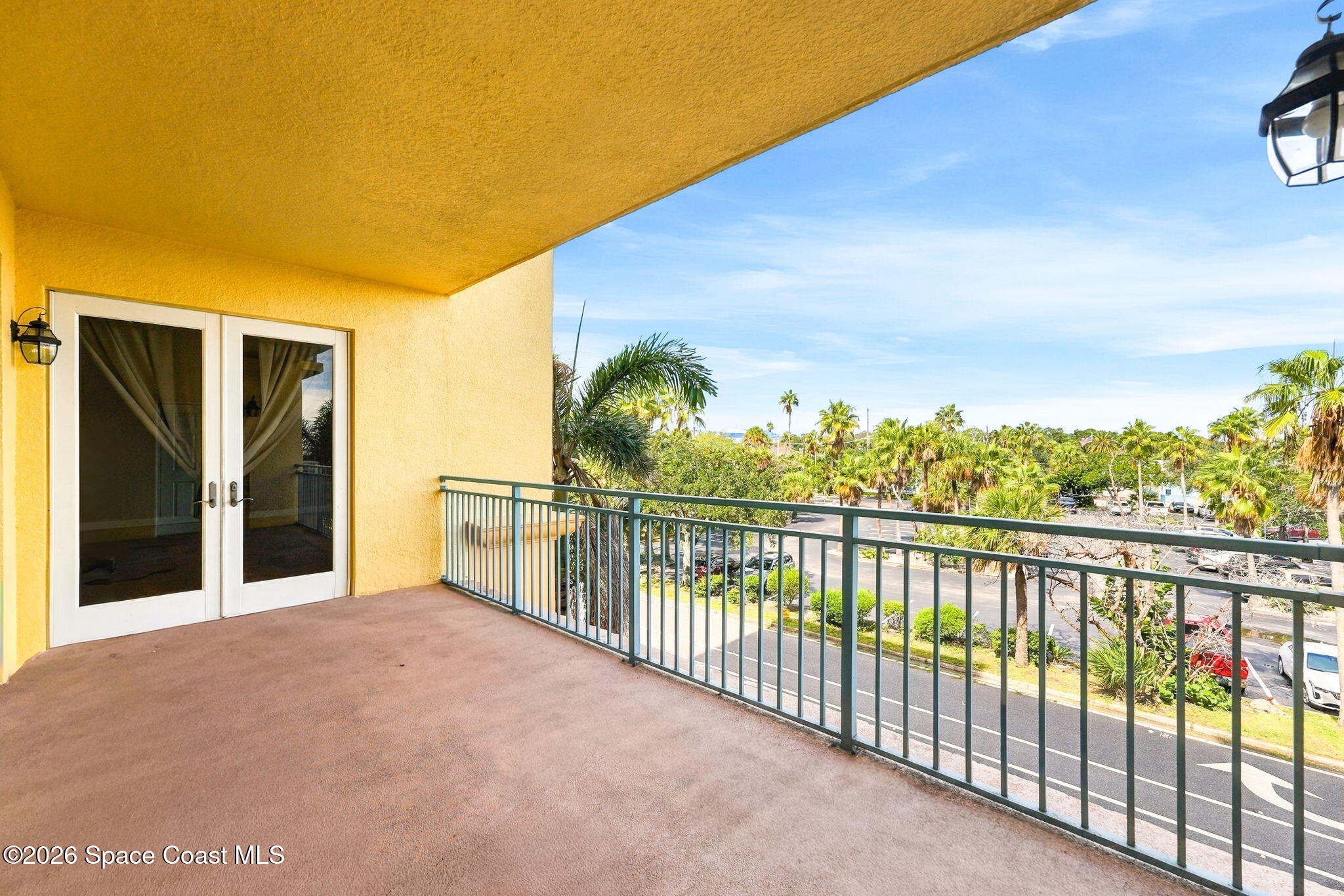 Covered condominium balcony overlooking palm trees, landscaping, and a parking area.