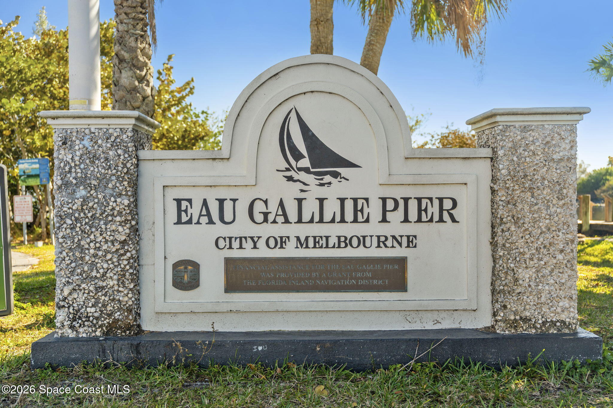 Eau Gallie Pier entrance sign in Melbourne, with a sailboat emblem and palm trees.
