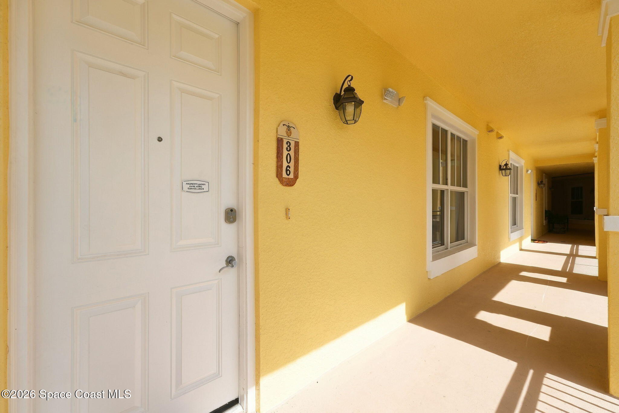 Condo unit 306 entrance along a sunny yellow stucco corridor with windows and lantern lights.
