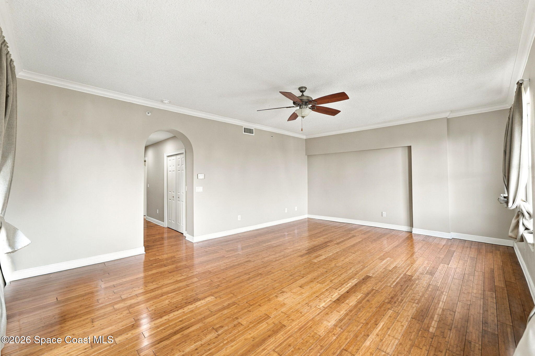 Empty living room with polished hardwood floors, an arched doorway, and a ceiling fan.