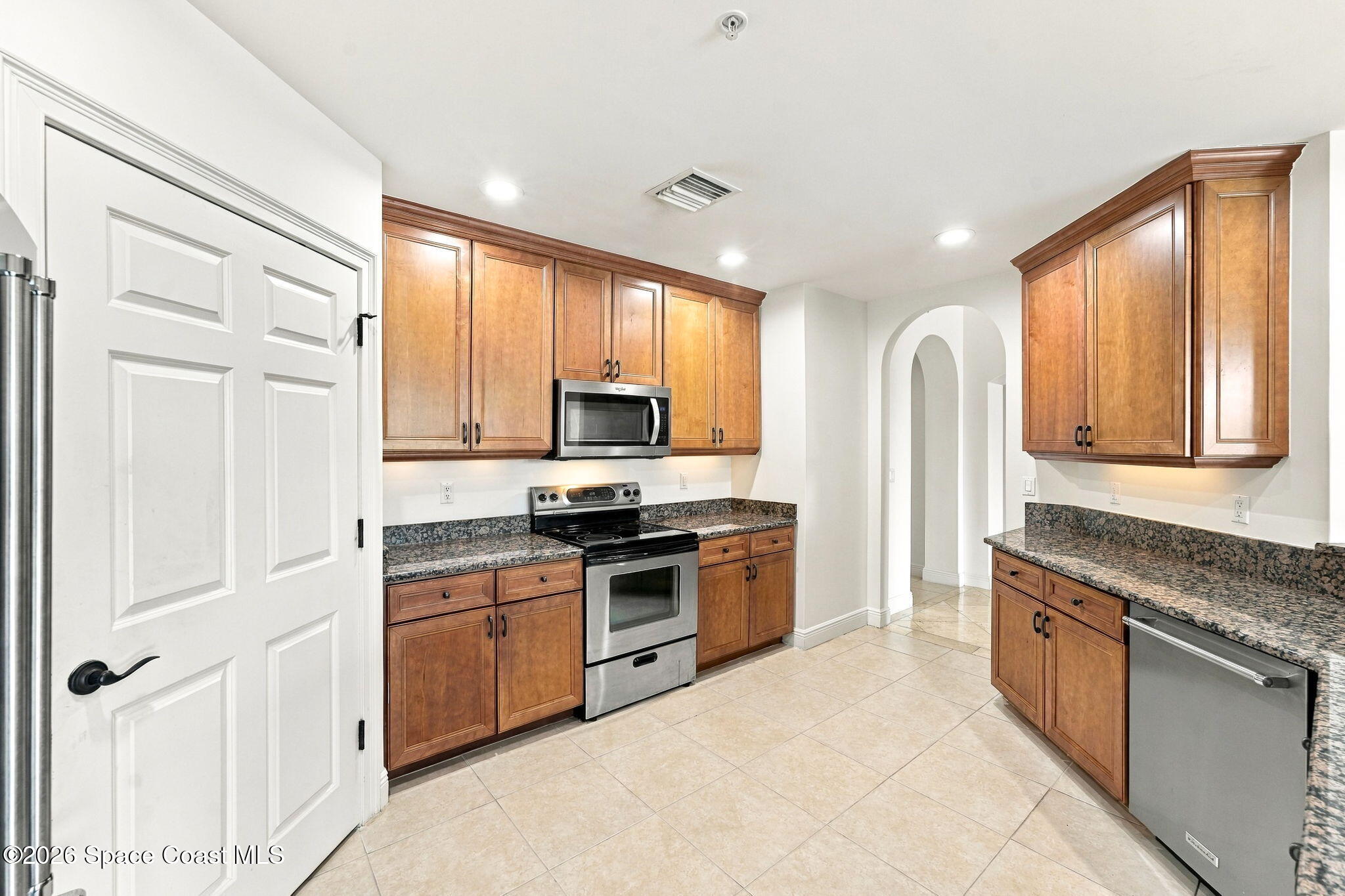 Kitchen with warm wood cabinets, granite countertops, stainless steel appliances, and an arched doorway.