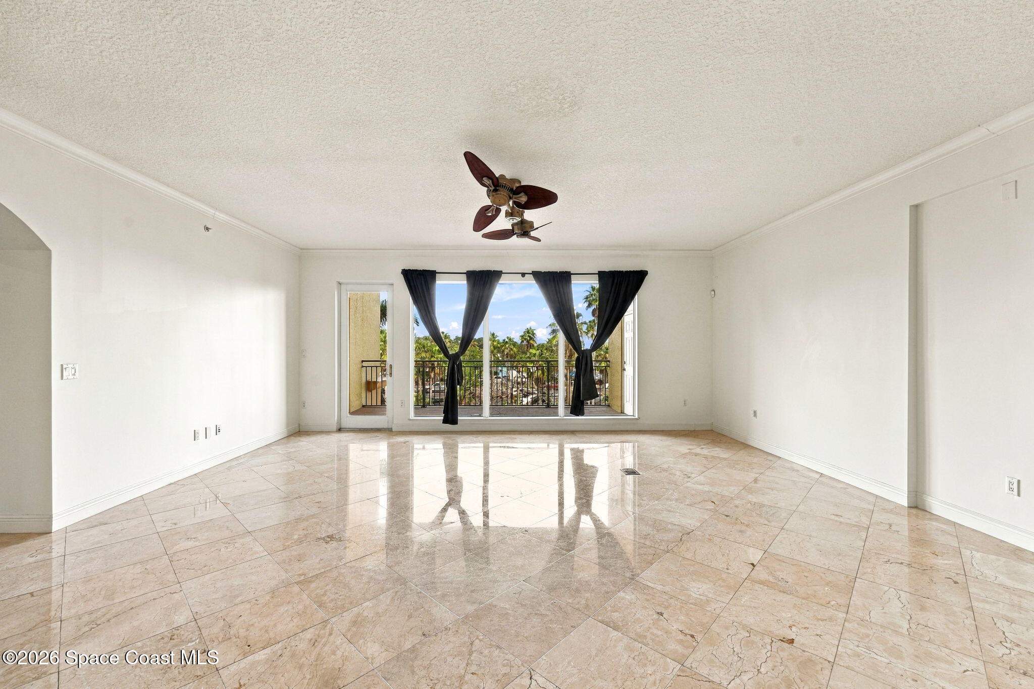 Vacant living room with glossy tile floors and sliding doors opening to a palm-lined view.