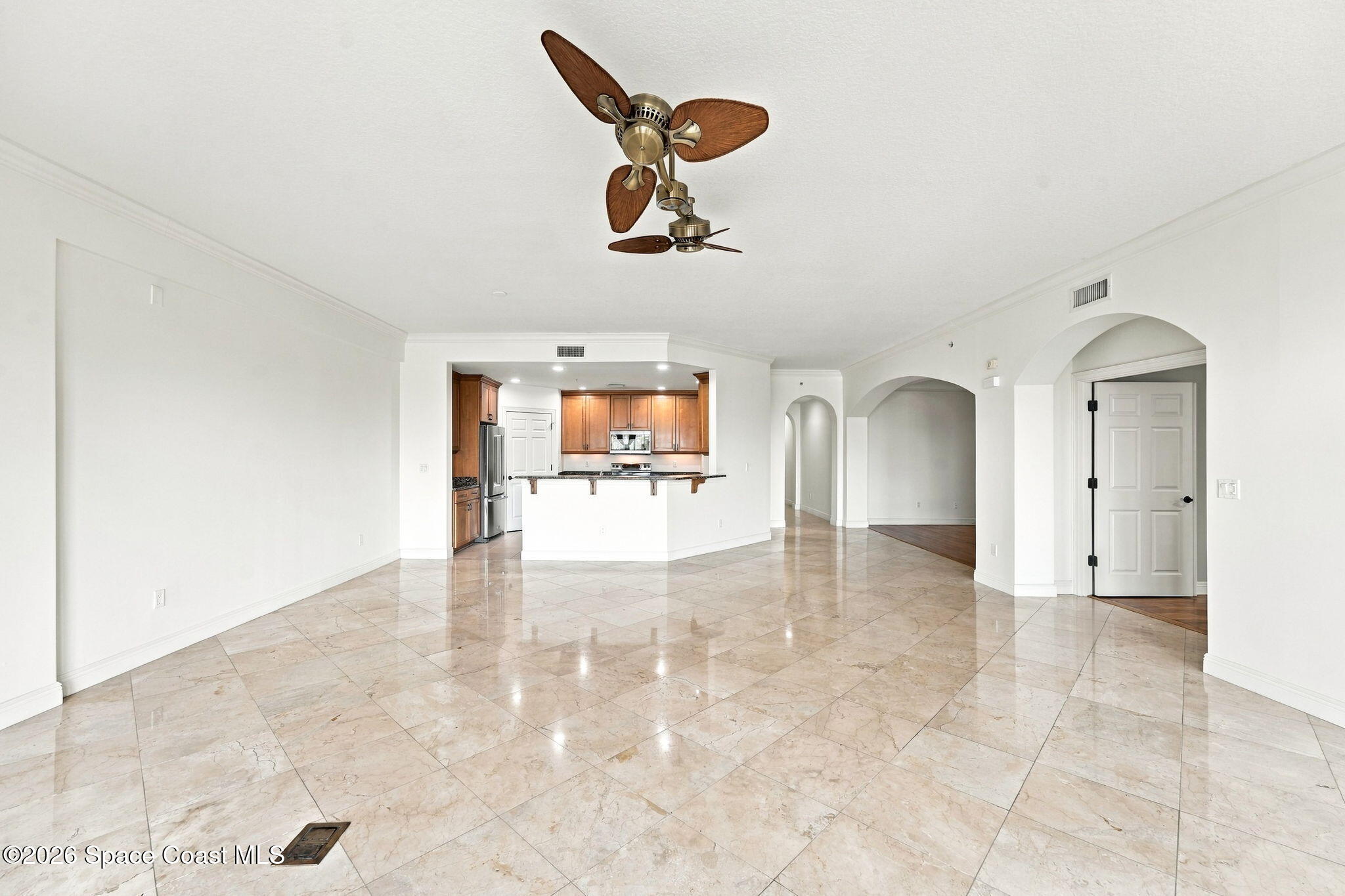Open living area with glossy marble tile floors, arched openings, and a wood-cabinet kitchen.