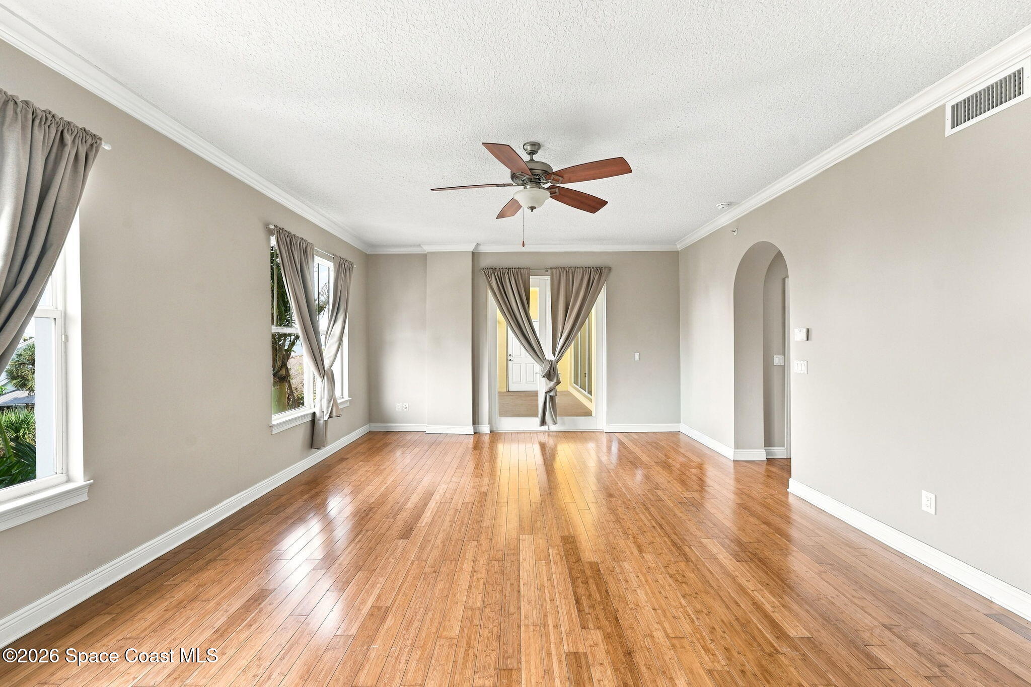 Vacant living room with polished hardwood floors, curtained windows, ceiling fan, and arched doorway.