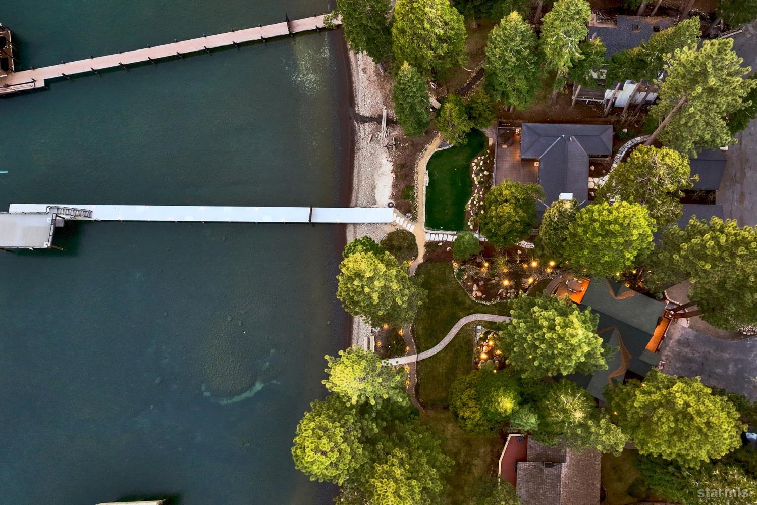 Aerial view of a lakefront home with two docks, landscaped grounds, and a rocky shoreline.