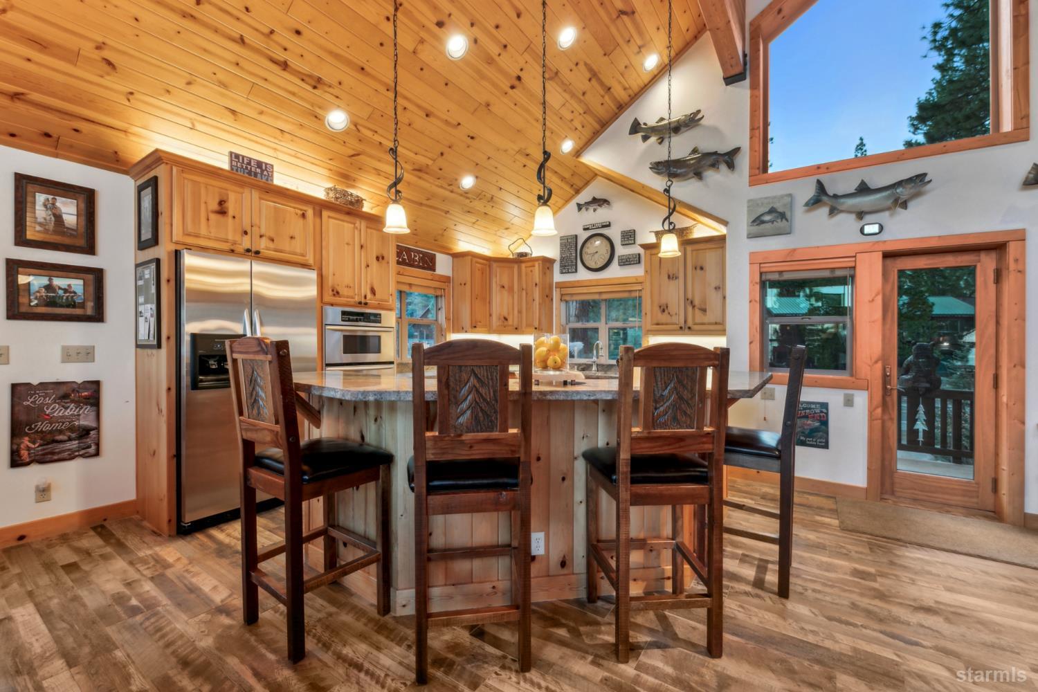 Kitchen with a large pine island, dark bar stools, vaulted wood ceiling, and glass doors to a deck.