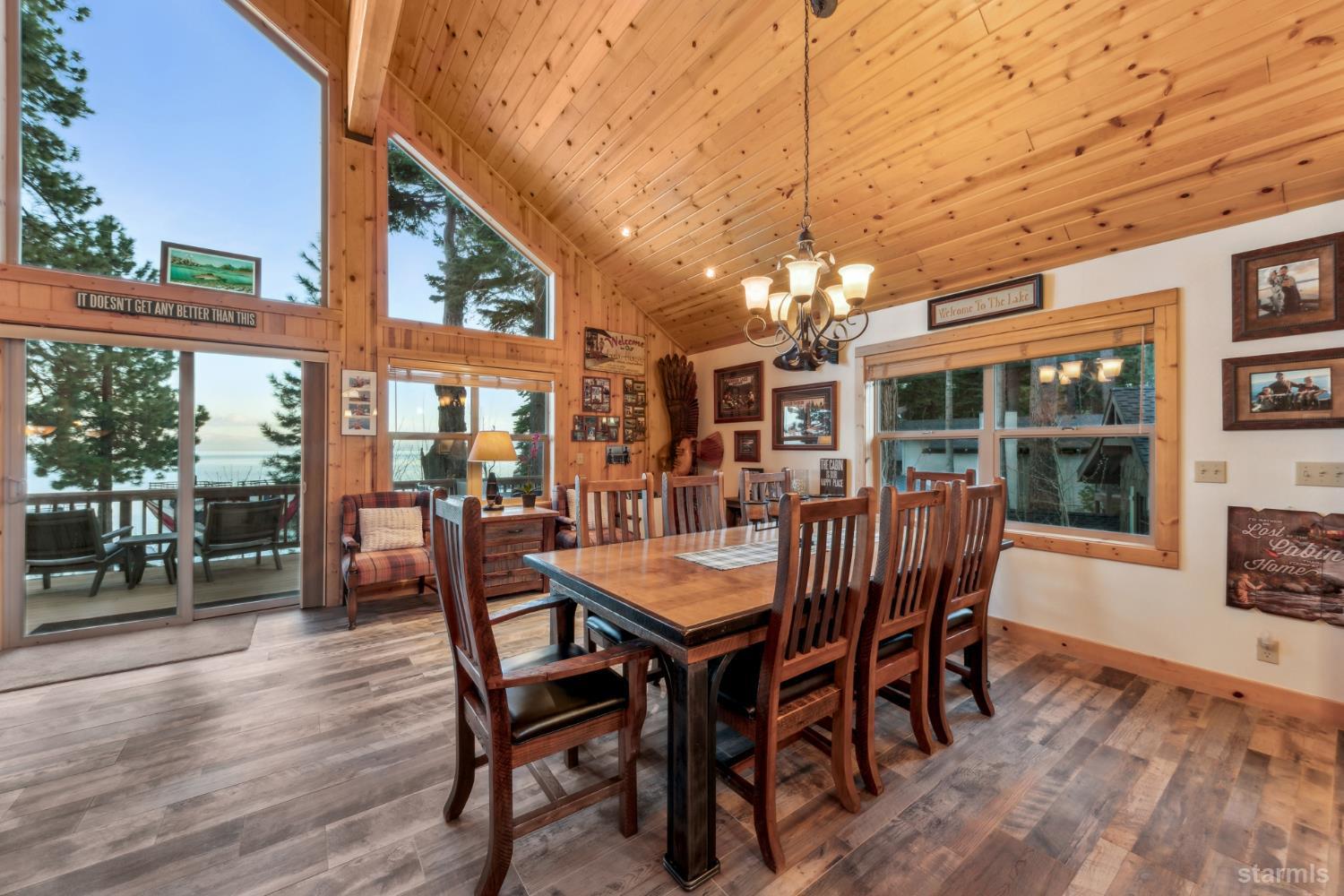 Dining room with a vaulted pine ceiling, wooden table, and windows overlooking the lake.