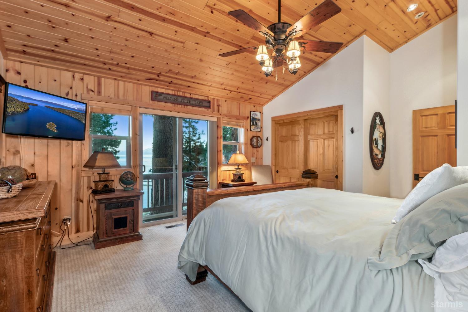 Bedroom with a vaulted wood ceiling, large bed, and lake views through sliding glass doors.