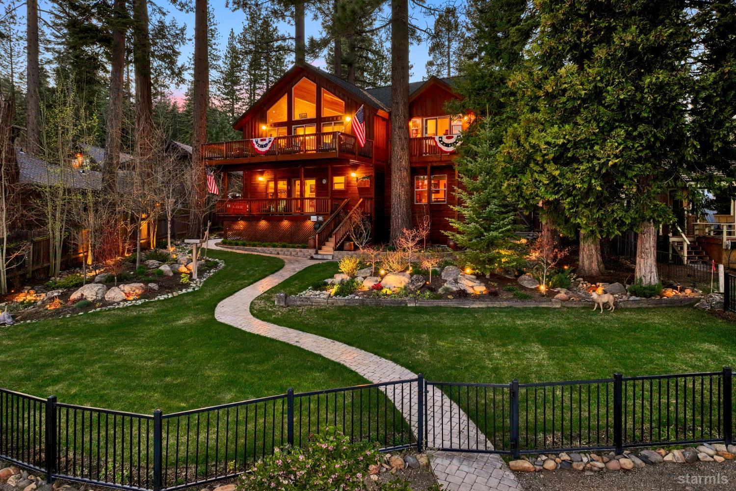 Wood-sided cabin among evergreens, with illuminated balconies and a curved stone path through the landscaped yard.
