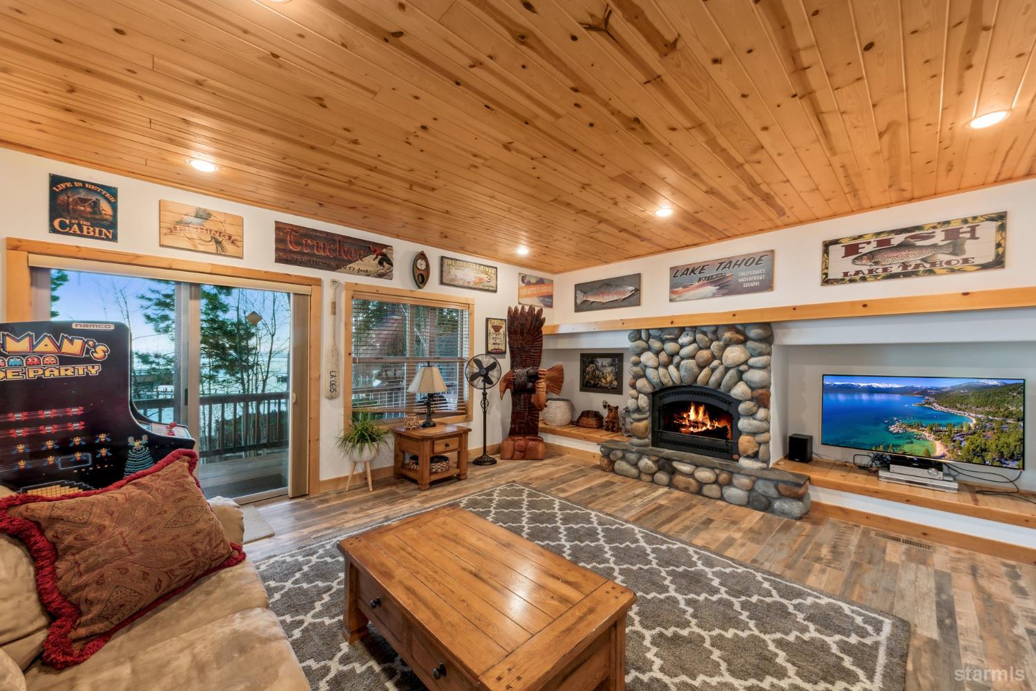Cabin-style living room with a stone fireplace, knotty-pine ceiling, and arcade game.