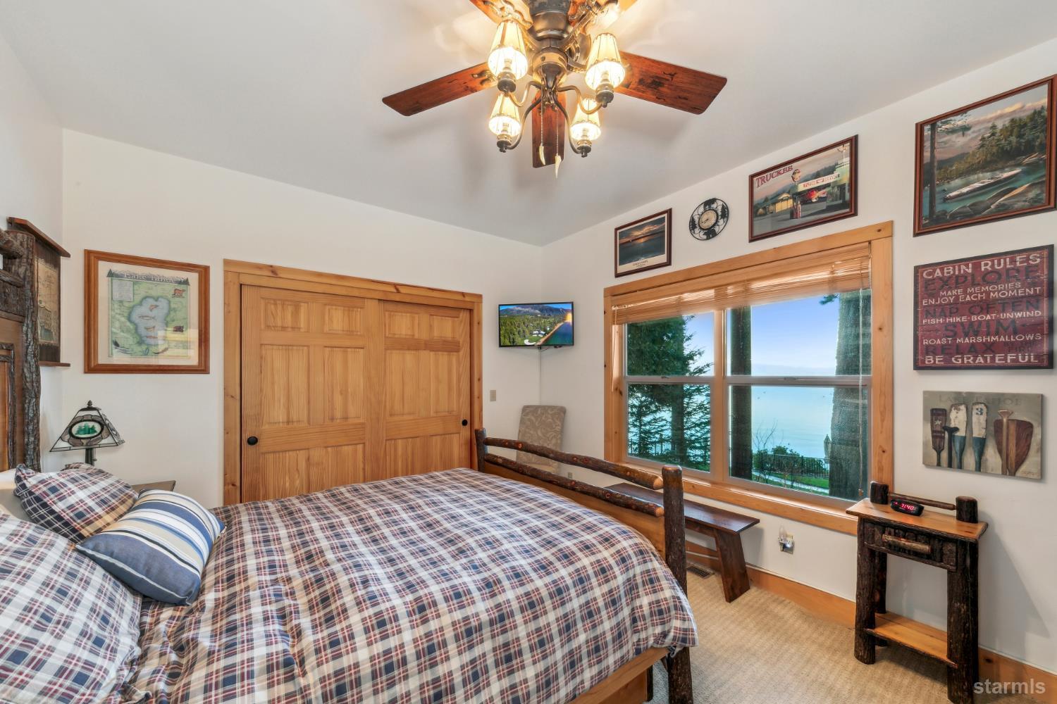 Bedroom with plaid bedding, rustic wood furnishings, and a large window overlooking the lake.