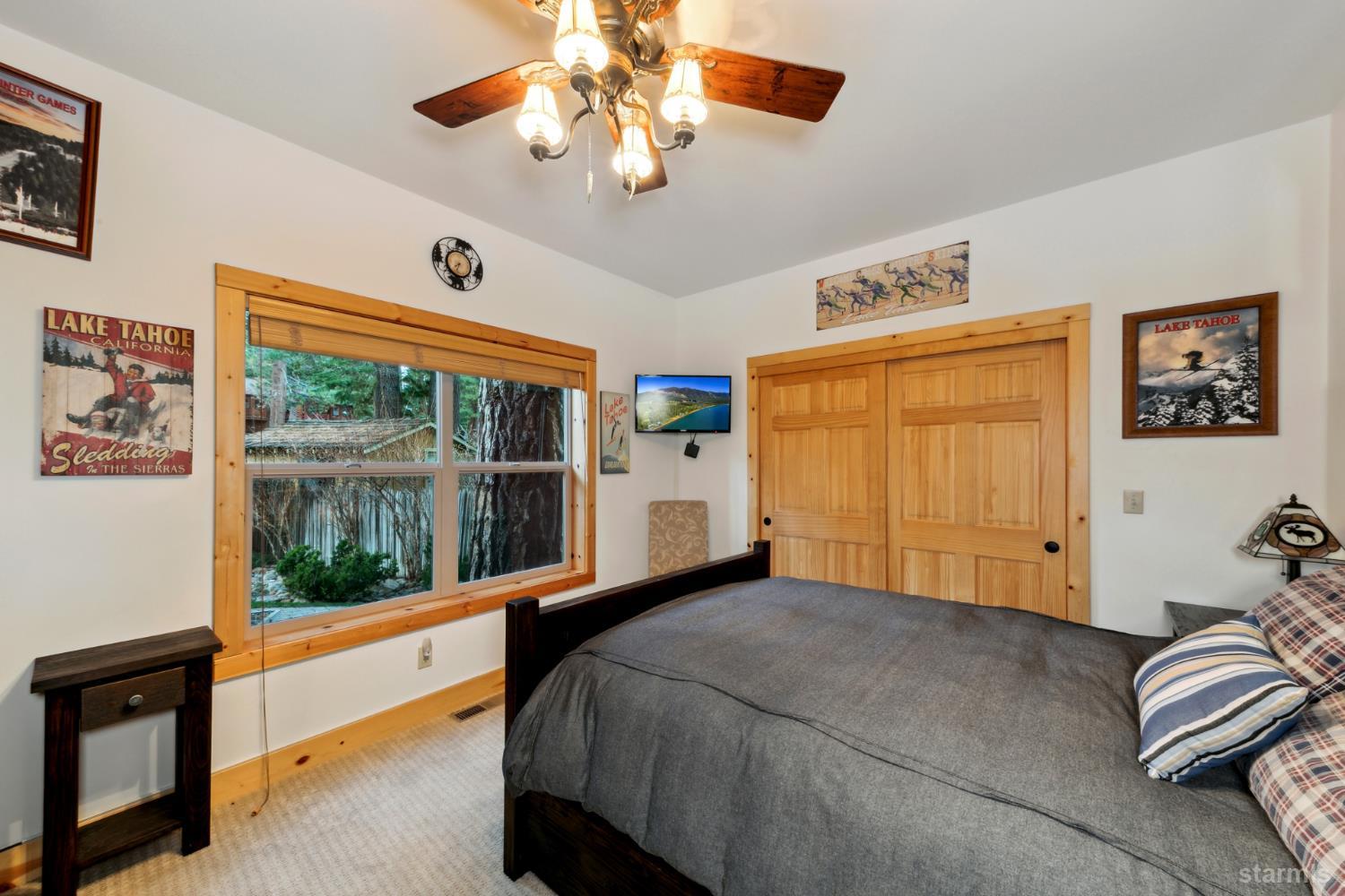 Bedroom with a large bed, wood-trimmed window overlooking trees, and sliding wooden closet doors.