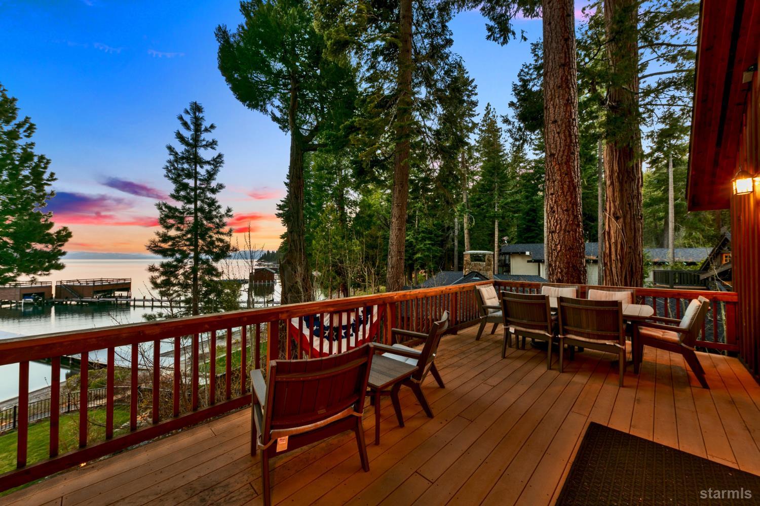Furnished lakeside deck overlooking the water and dock among tall pines at sunset.