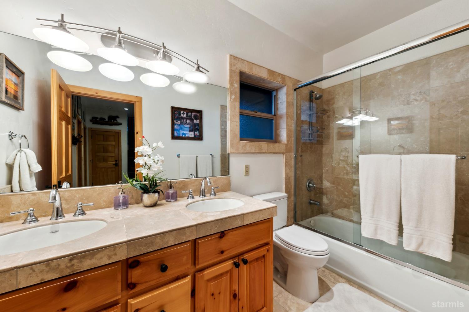 Bathroom with a double-sink vanity and glass-enclosed tub and shower.