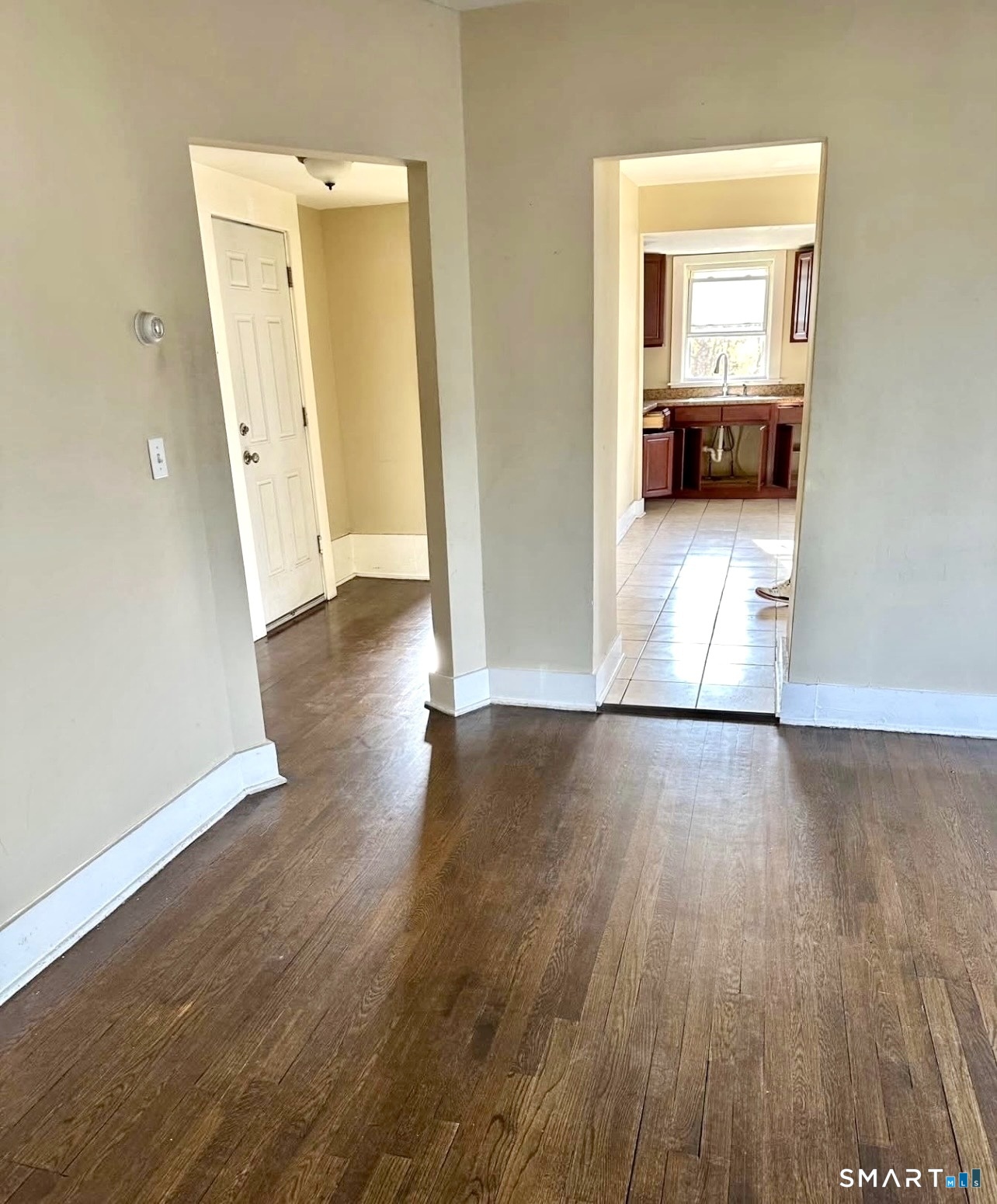Empty room with hardwood floors and doorways leading to a tiled kitchen.
