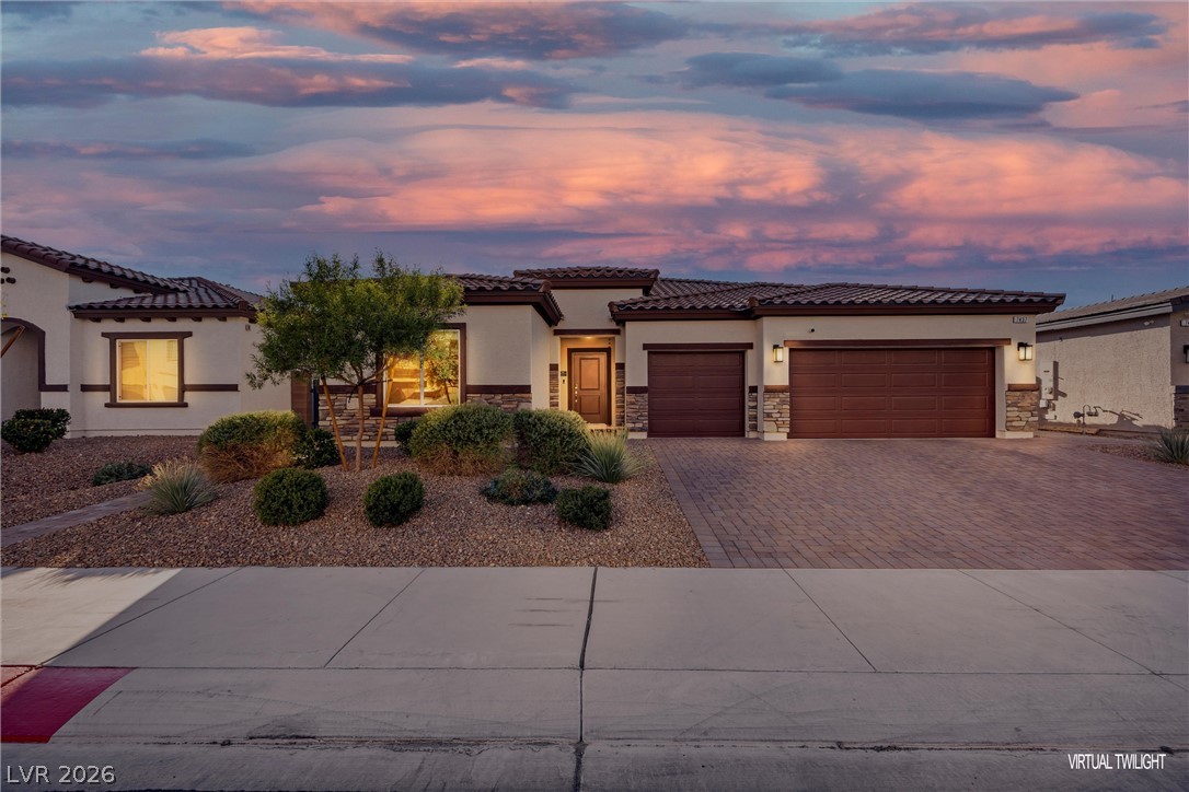 Single-story stucco home with a two-car garage and desert landscaping beneath a colorful dusk sky.