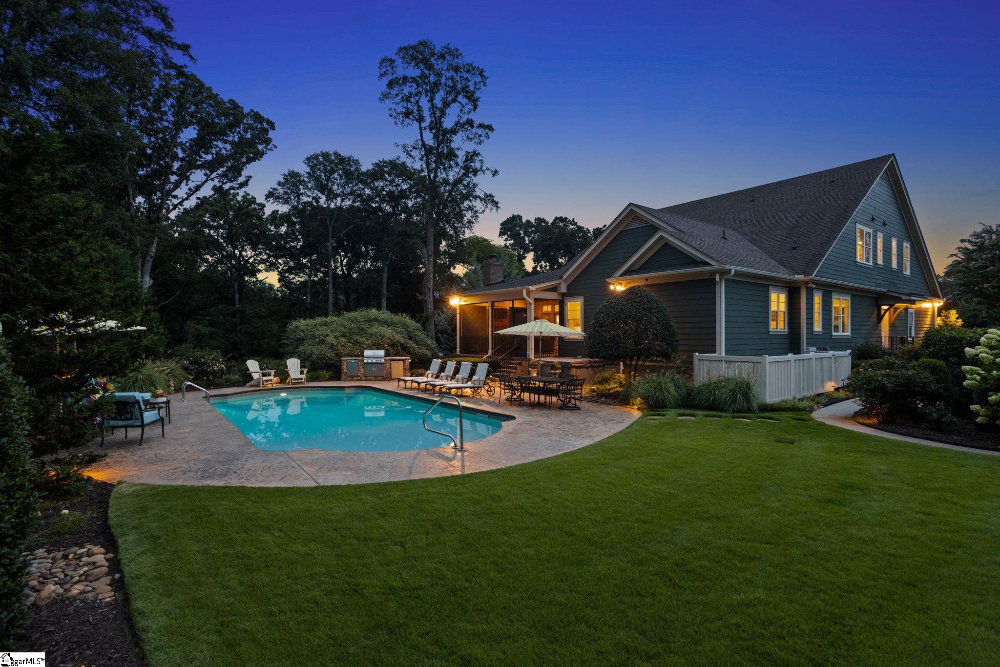 House and landscaped backyard with a swimming pool and patio at dusk.