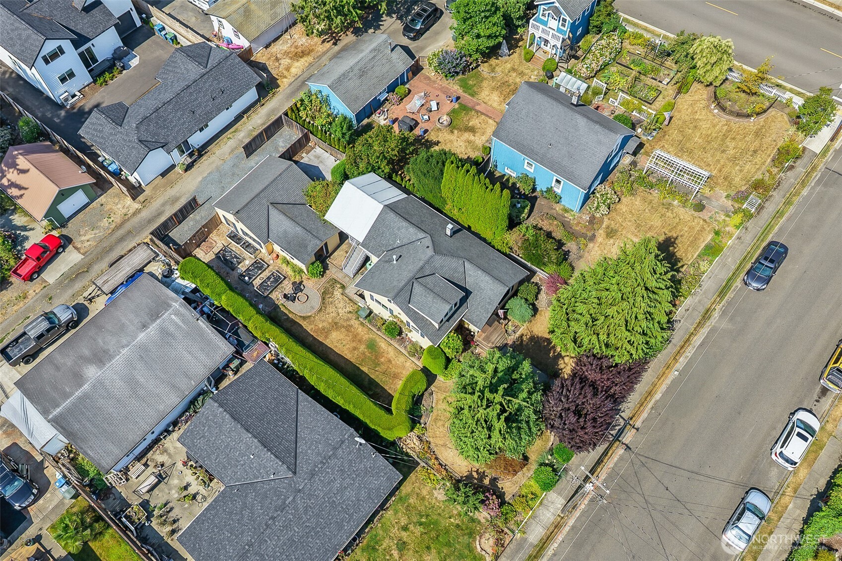 Aerial view of a house with a landscaped yard, patio, and mature trees among neighboring homes.