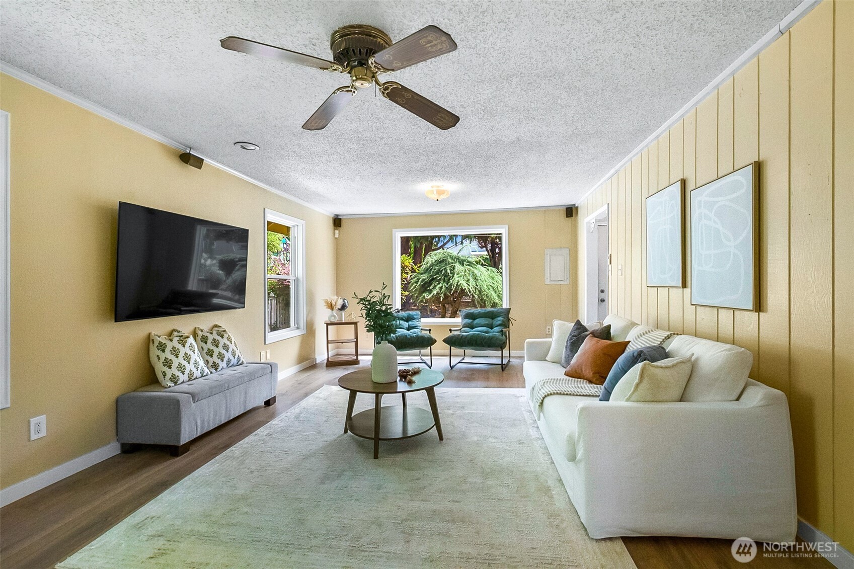 Living room with yellow walls, white sofa, teal armchairs, and a large window overlooking greenery.