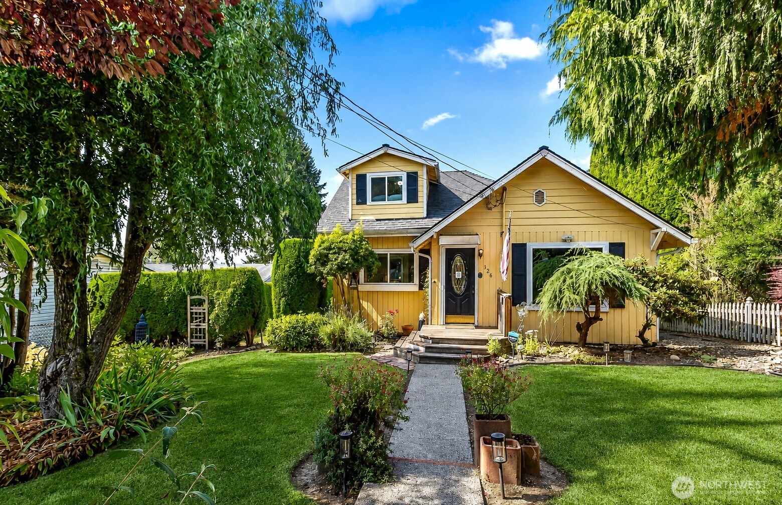 Yellow house with a dormer and dark front door, approached by a garden path through a landscaped lawn.