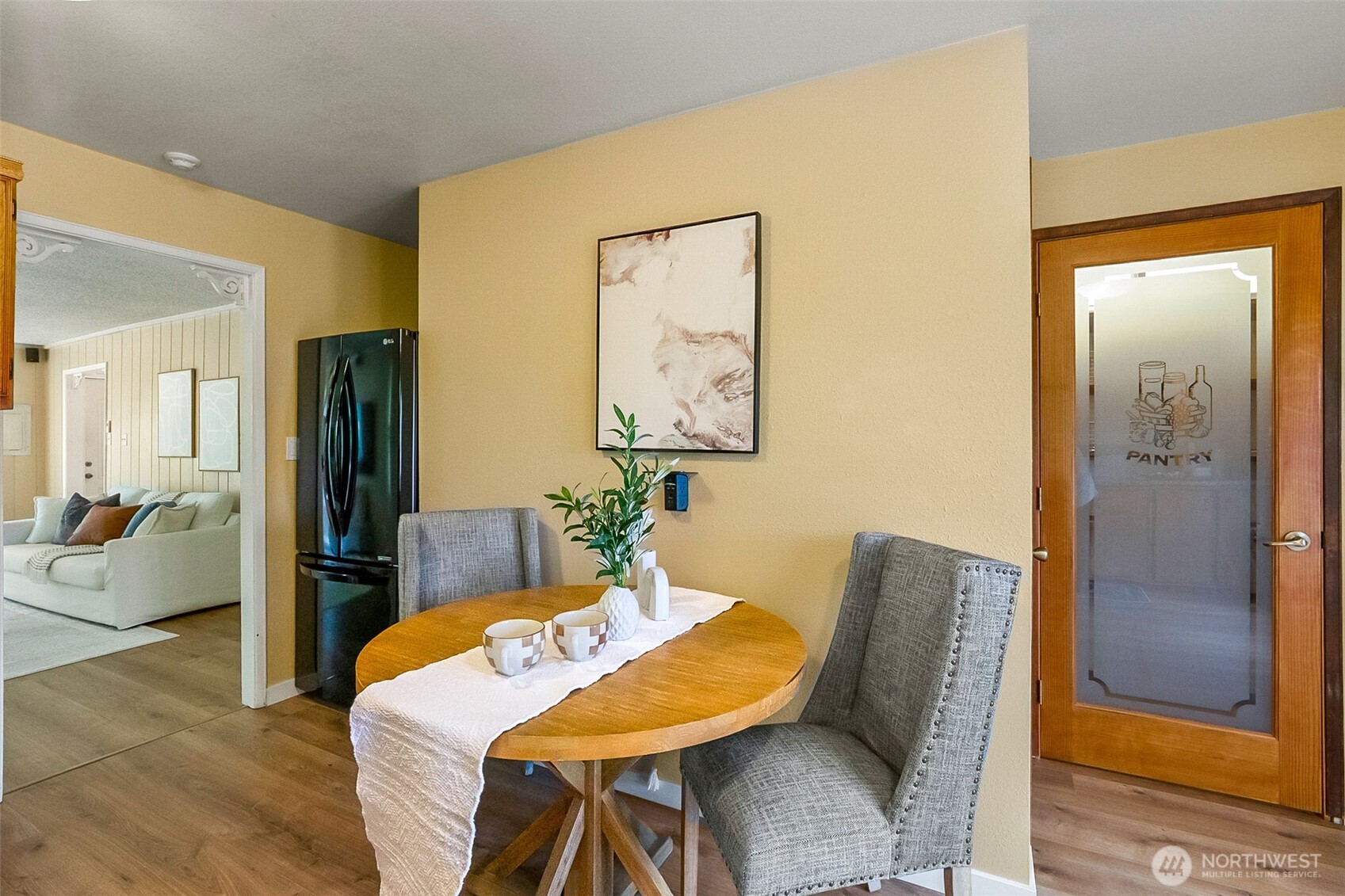 Dining area with a round wooden table, gray chairs, and a frosted-glass pantry door.
