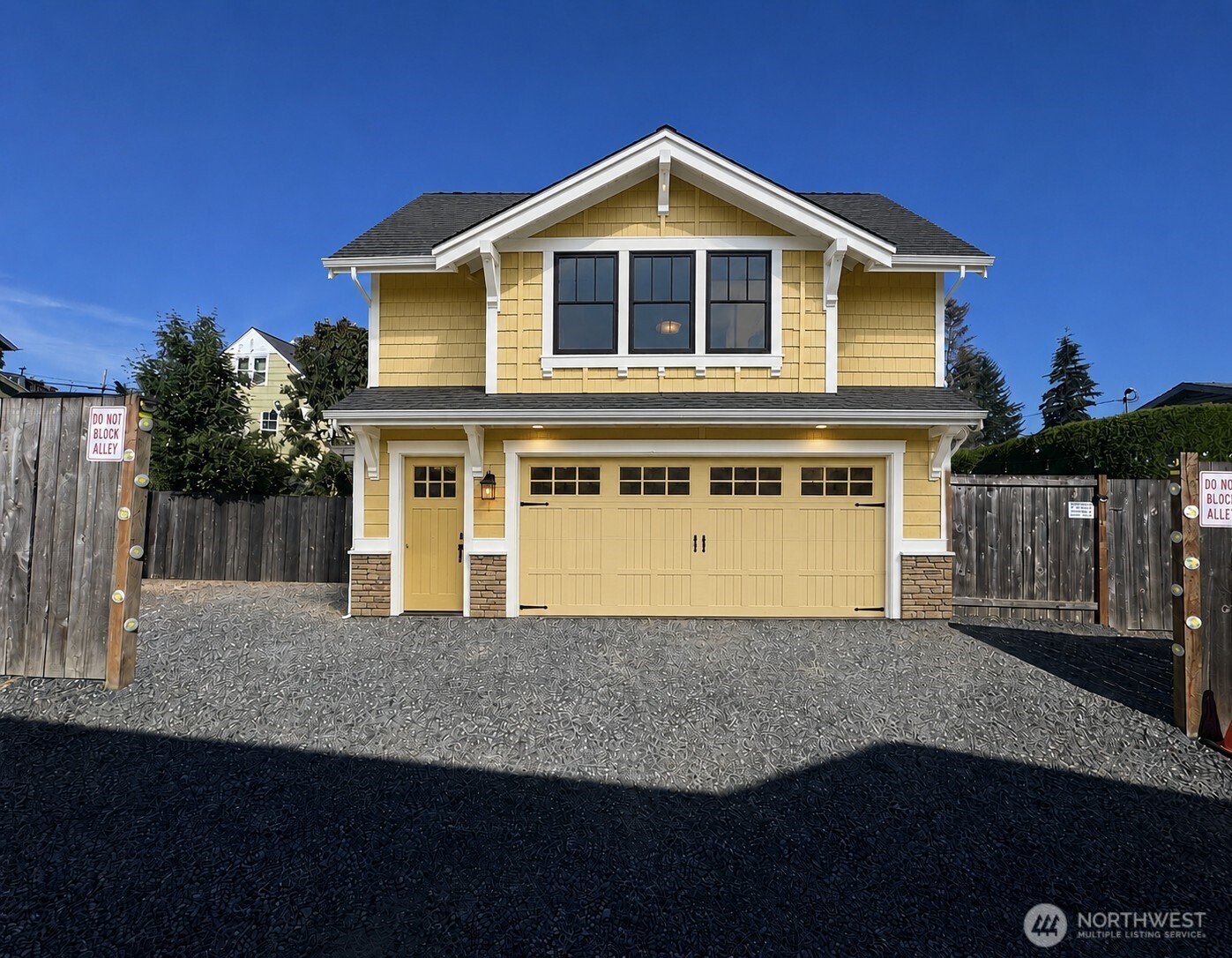 Yellow two-story house with a prominent front gable and wide garage door, viewed from the alley.
