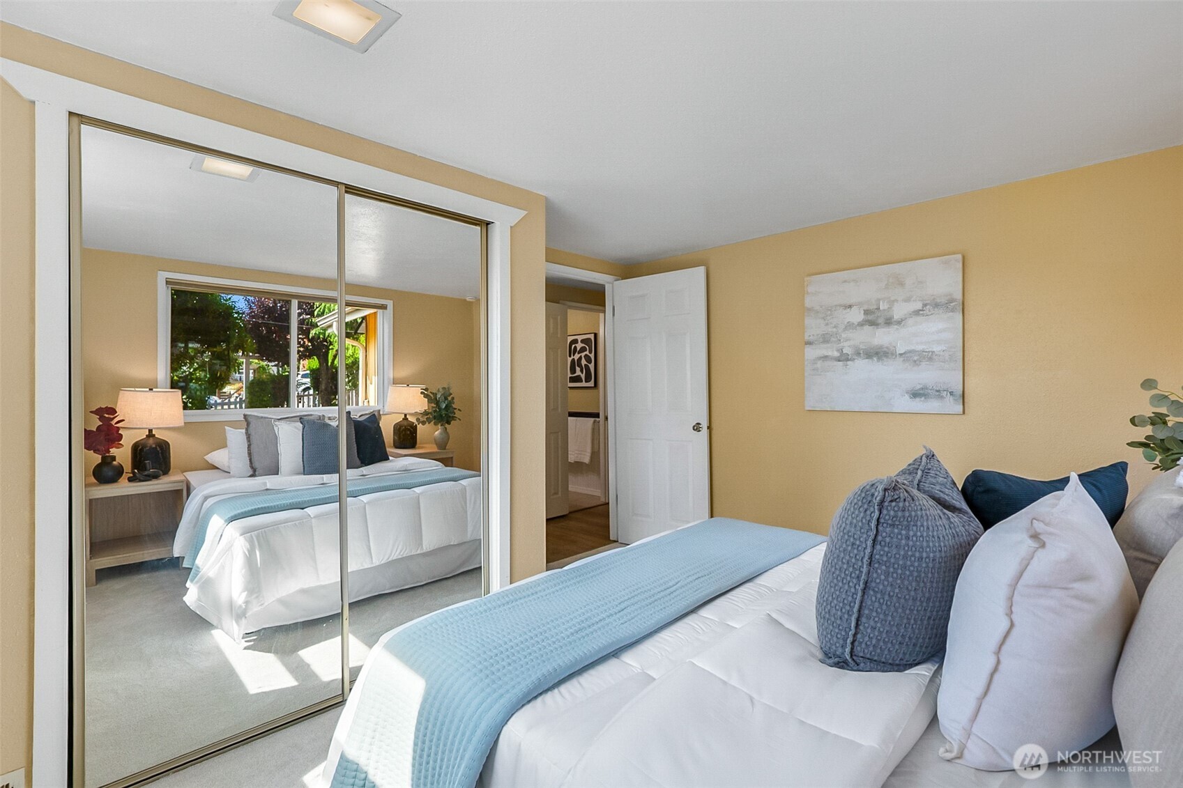 Staged bedroom with a white bed, pale blue coverlet, and mirrored sliding closet doors.