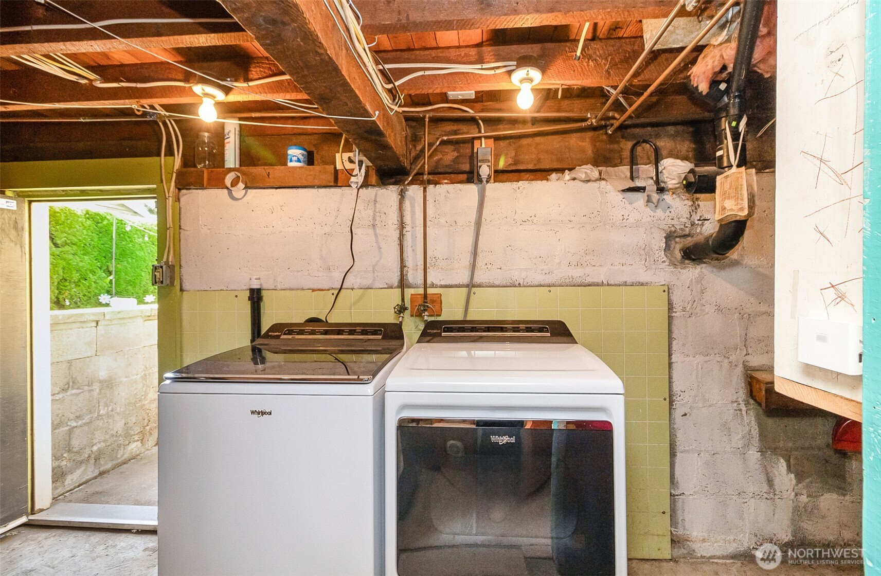 Basement laundry area with a washer and dryer, exposed beams, and concrete walls.