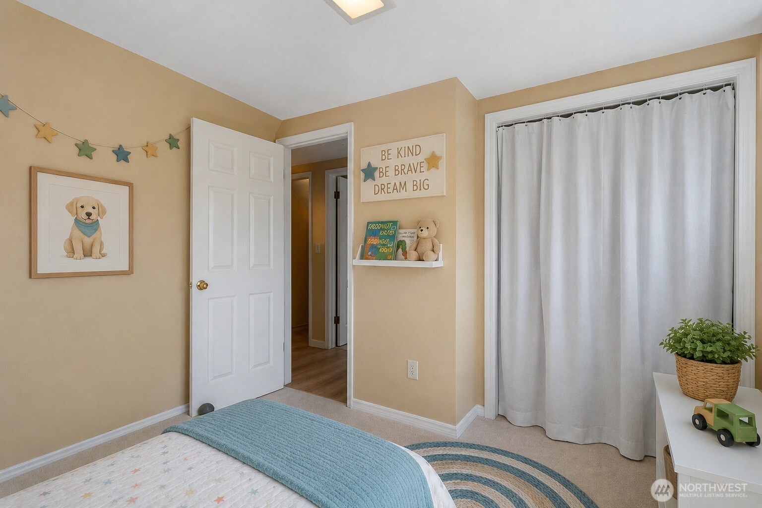 Child's bedroom with a teal bed blanket, star decorations, and a “Be Kind, Be Brave, Dream Big” sign.